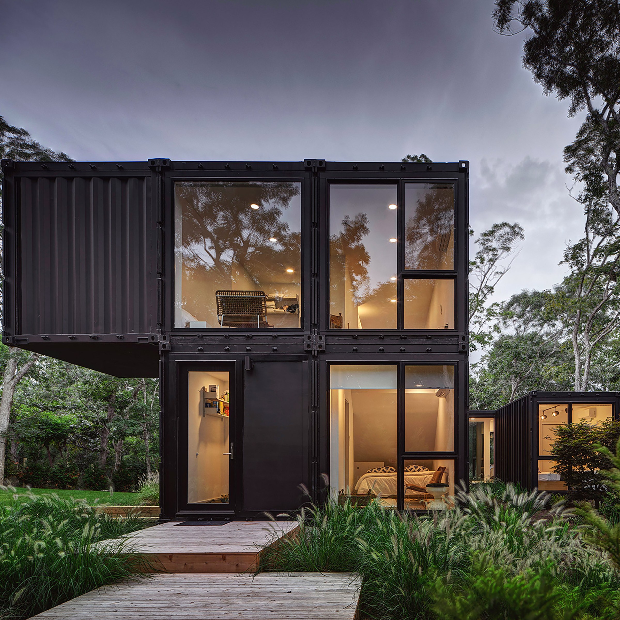 Black modern modular house with large windows and lush green trees surrounding 