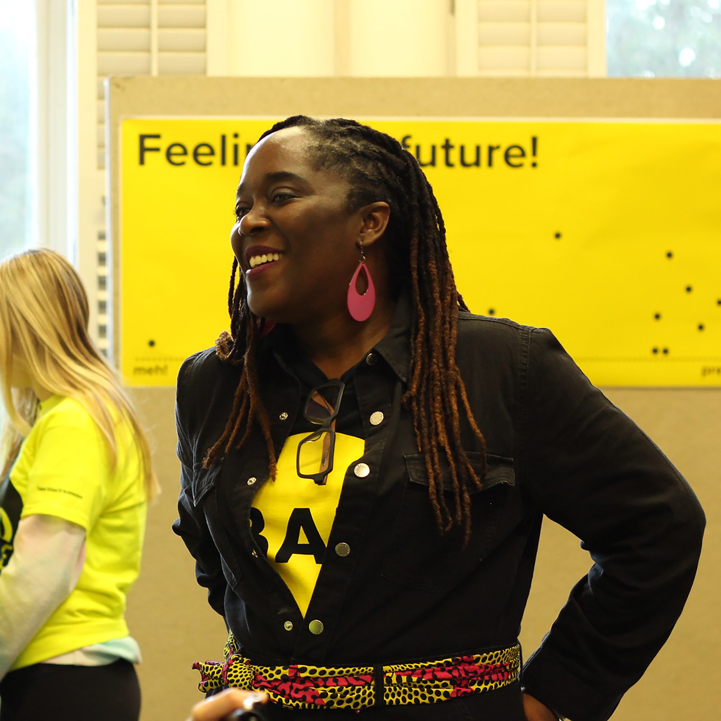 photo of woman standing in front of bright yellow sign with another woman in the background