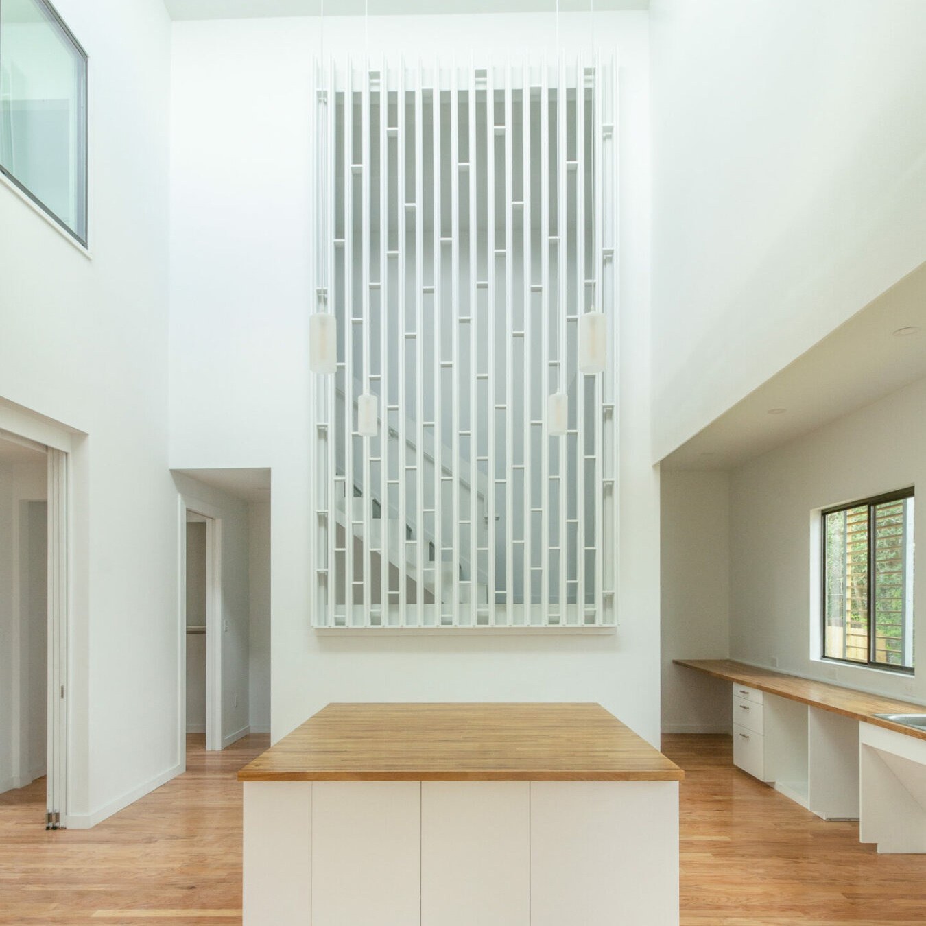 Interior of high-ceiling kitchen space with vertical-slat screen feature built in the foreground with staircase behind the screen