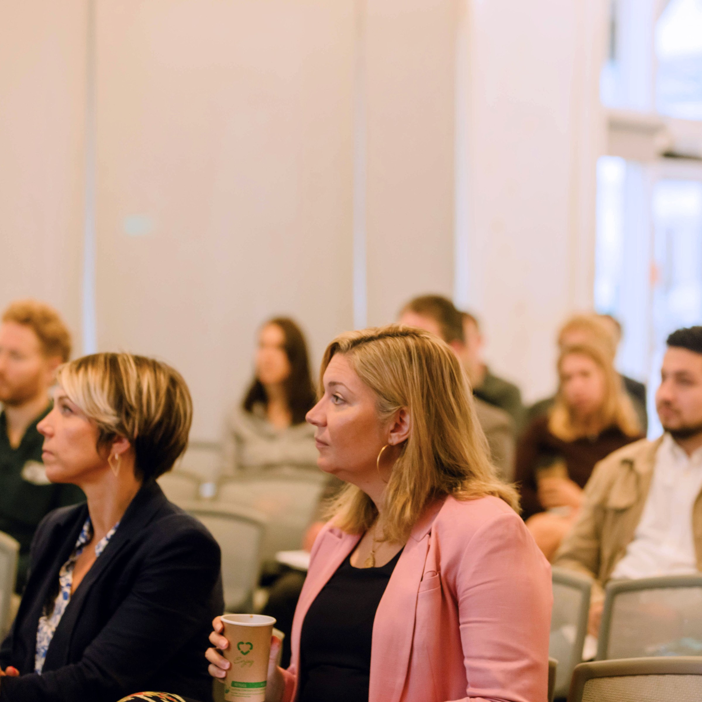 Photo of 7 rows of audience in chairs facing toward the camera, looking to the left side of the frame.