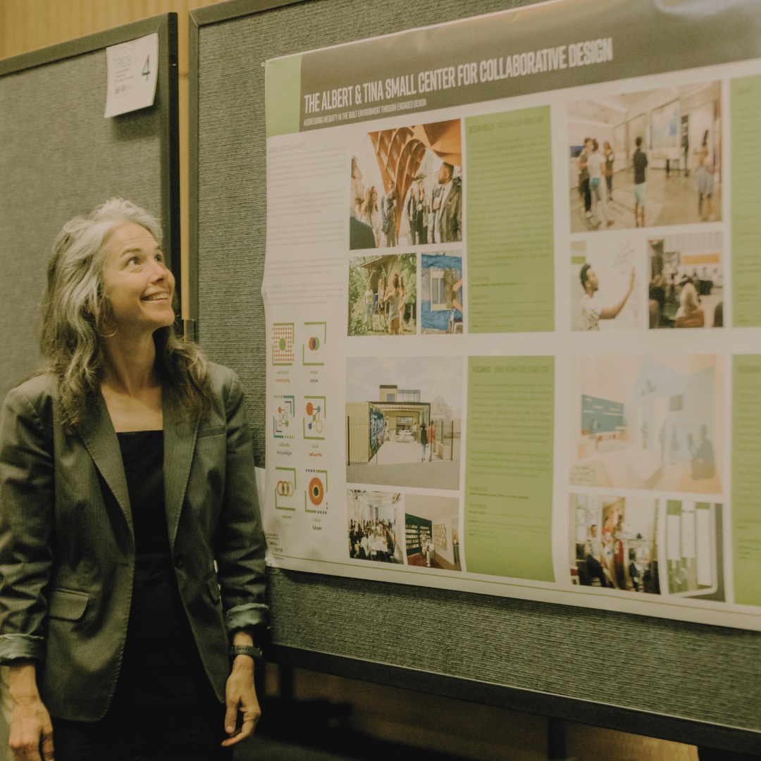 Faculty and Small Center Director Ann Yoachim stands next to a large poster that describes the work of the Small Center as Tulane's community-engaged design center.
