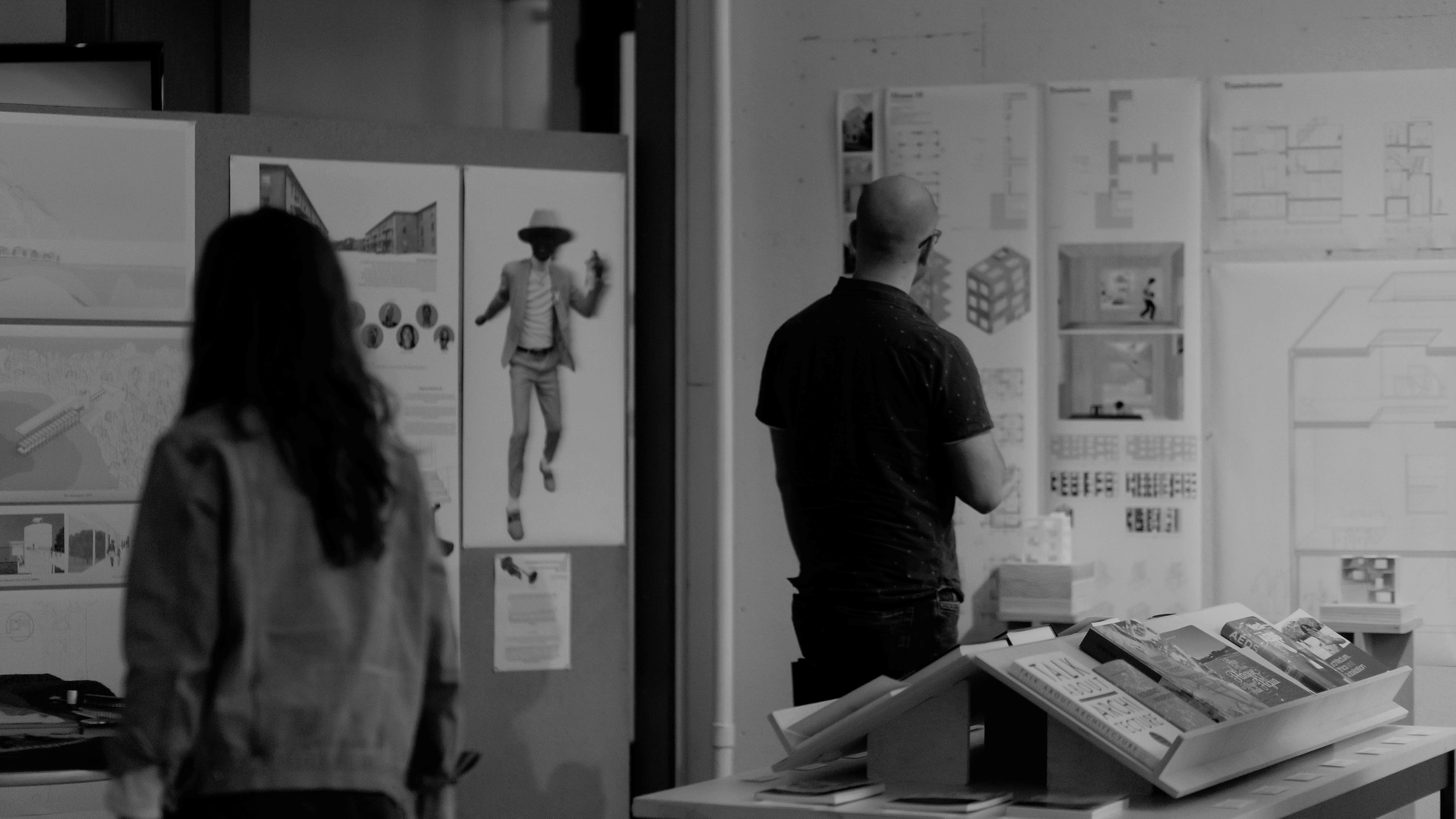 photo from behind two people looking at pin-up projects on walls in an open lobby