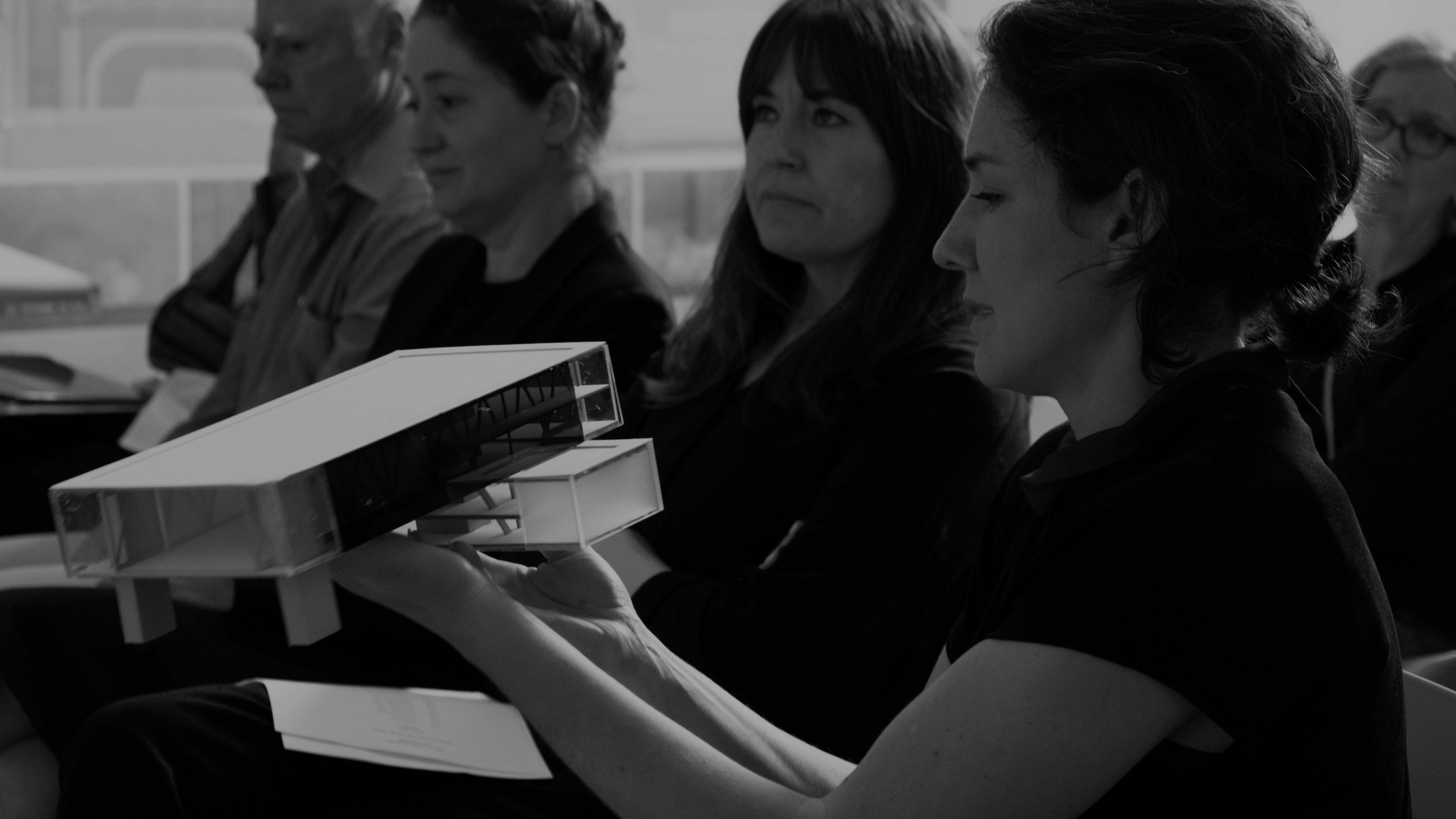 Photo of four people sitting and the one in the foreground is holding and looking at a model