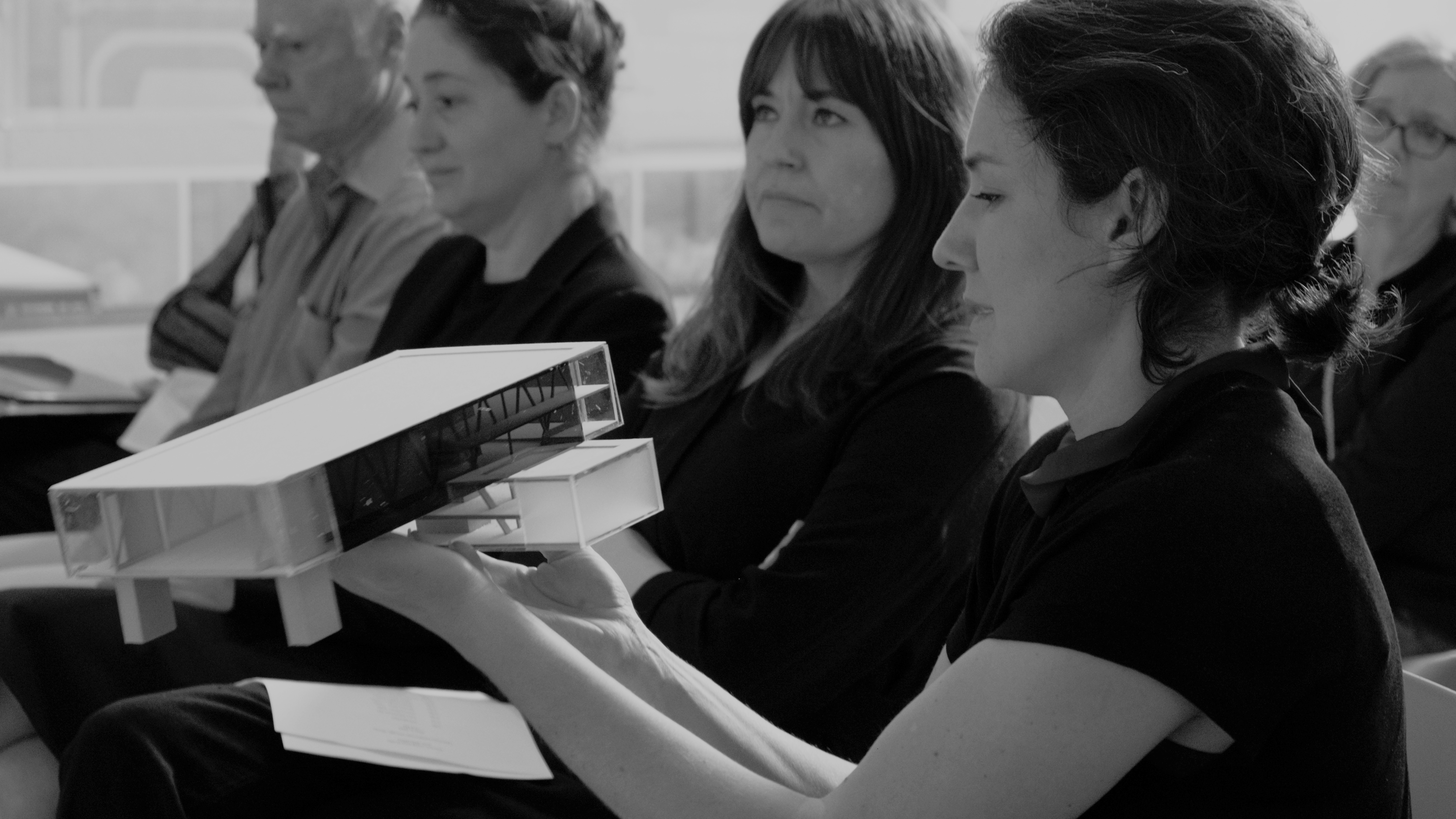 Photo of 4 people sitting and the one in the foreground is holding and looking at a model