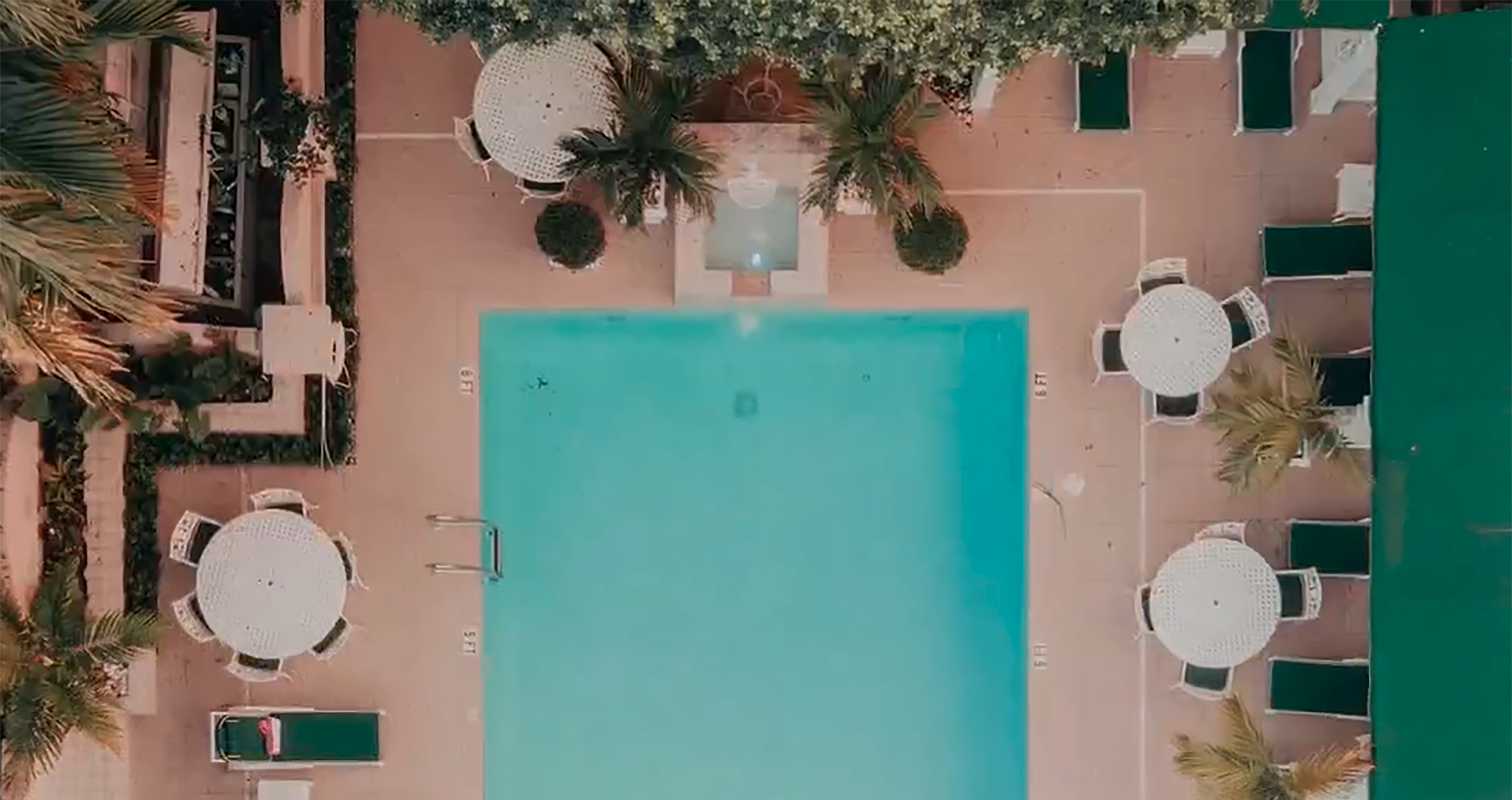 Aerial photo looking down at an empty pool surrounded by patio furniture and lush, tropical landscaping