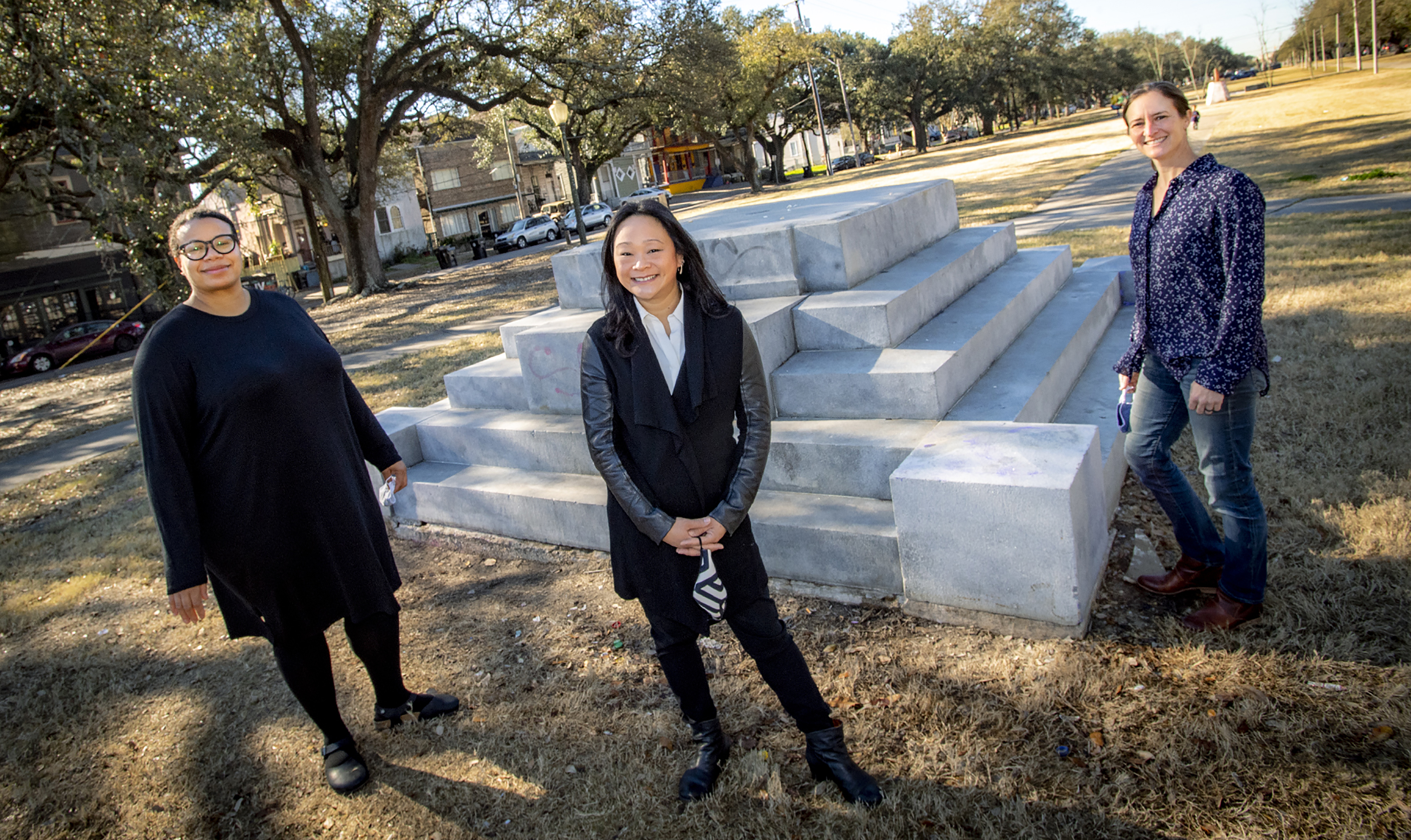 Photo of Tulane faculty Lisa Molix, Tiffany Lin, and Emilie Taylor Welty standing outside in a grassy neutral ground in front of a Confederate monument where the main structure or statue atop the pedestal has been removed.