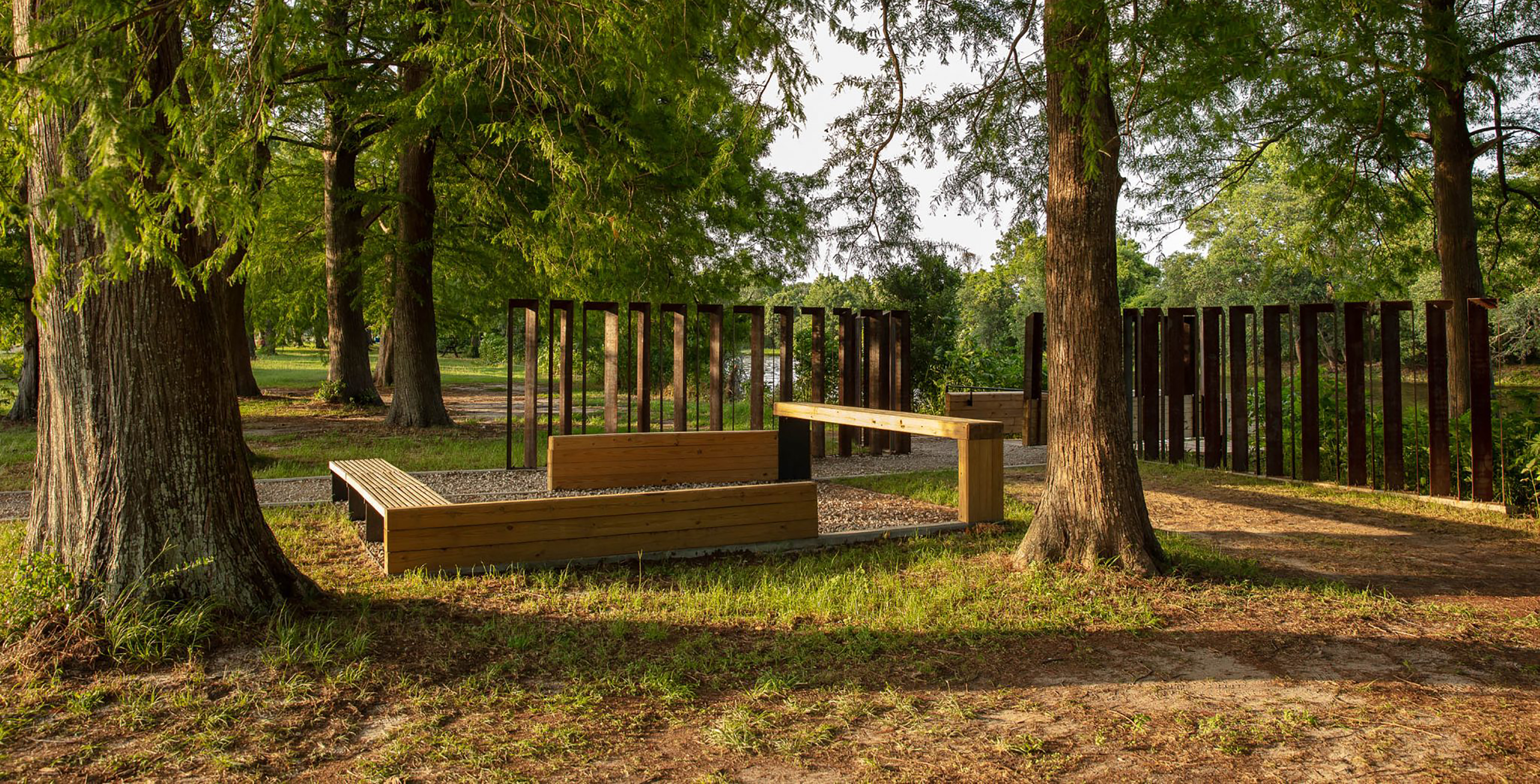 Photo of an outdoor gathering space with simple benches, trees in the foreground and water in the background