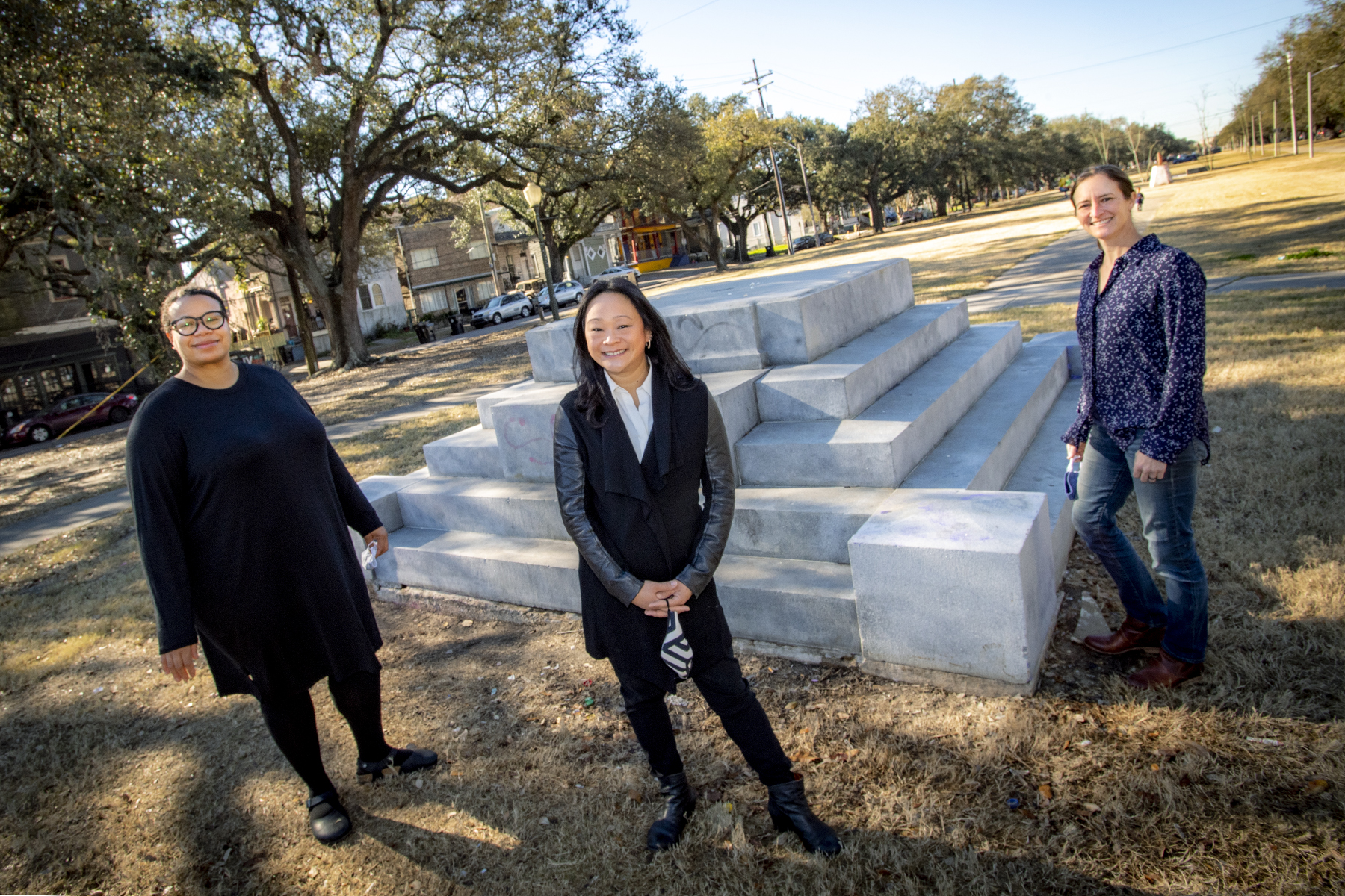Photo of Tulane faculty Lisa Molix, Tiffany Lin, and Emilie Taylor Welty standing outside in a grassy neutral ground in front of a Confederate monument where the main structure or statue atop the pedestal has been removed.
