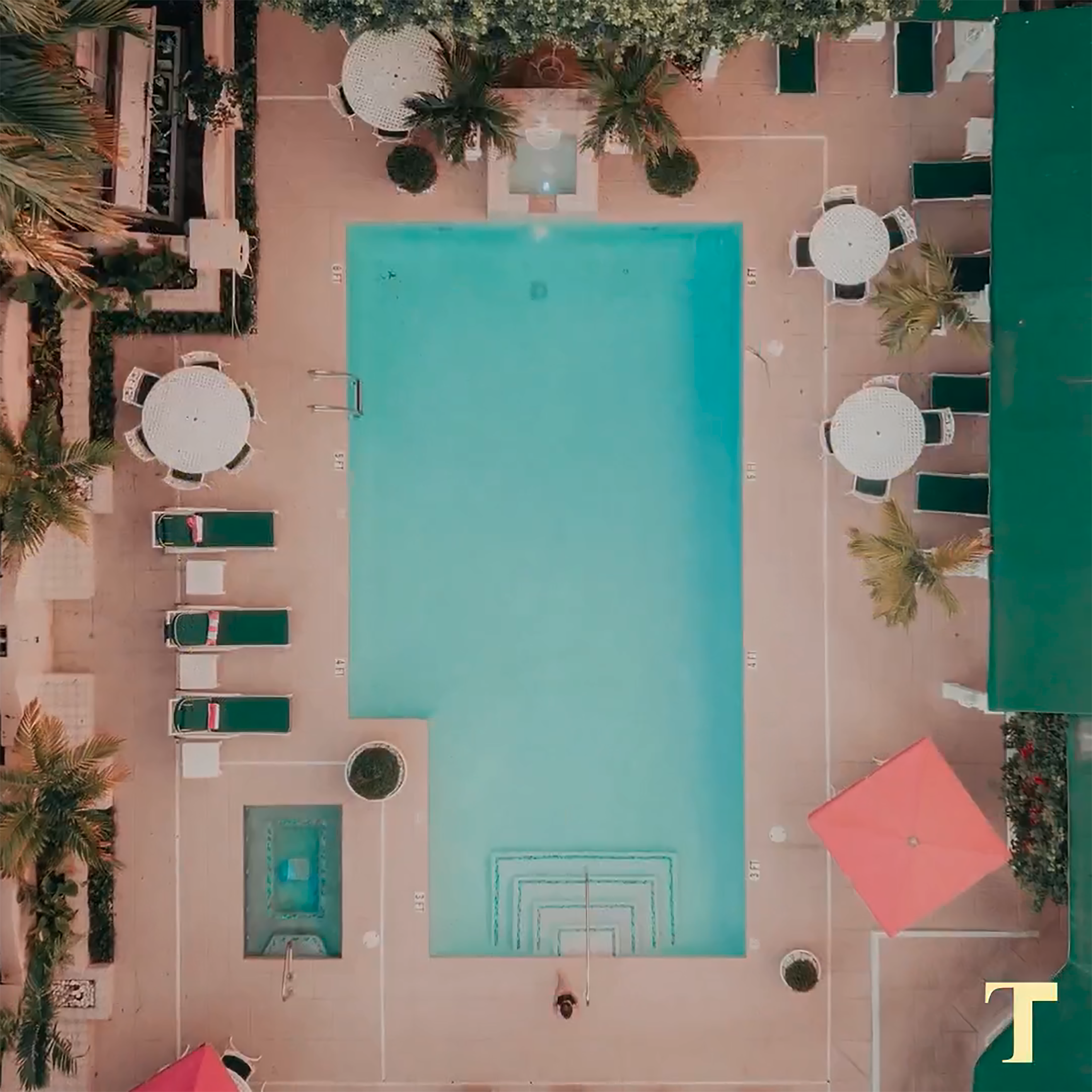 Aerial photo looking down at an empty pool surrounded by patio furniture and lush, tropical landscaping