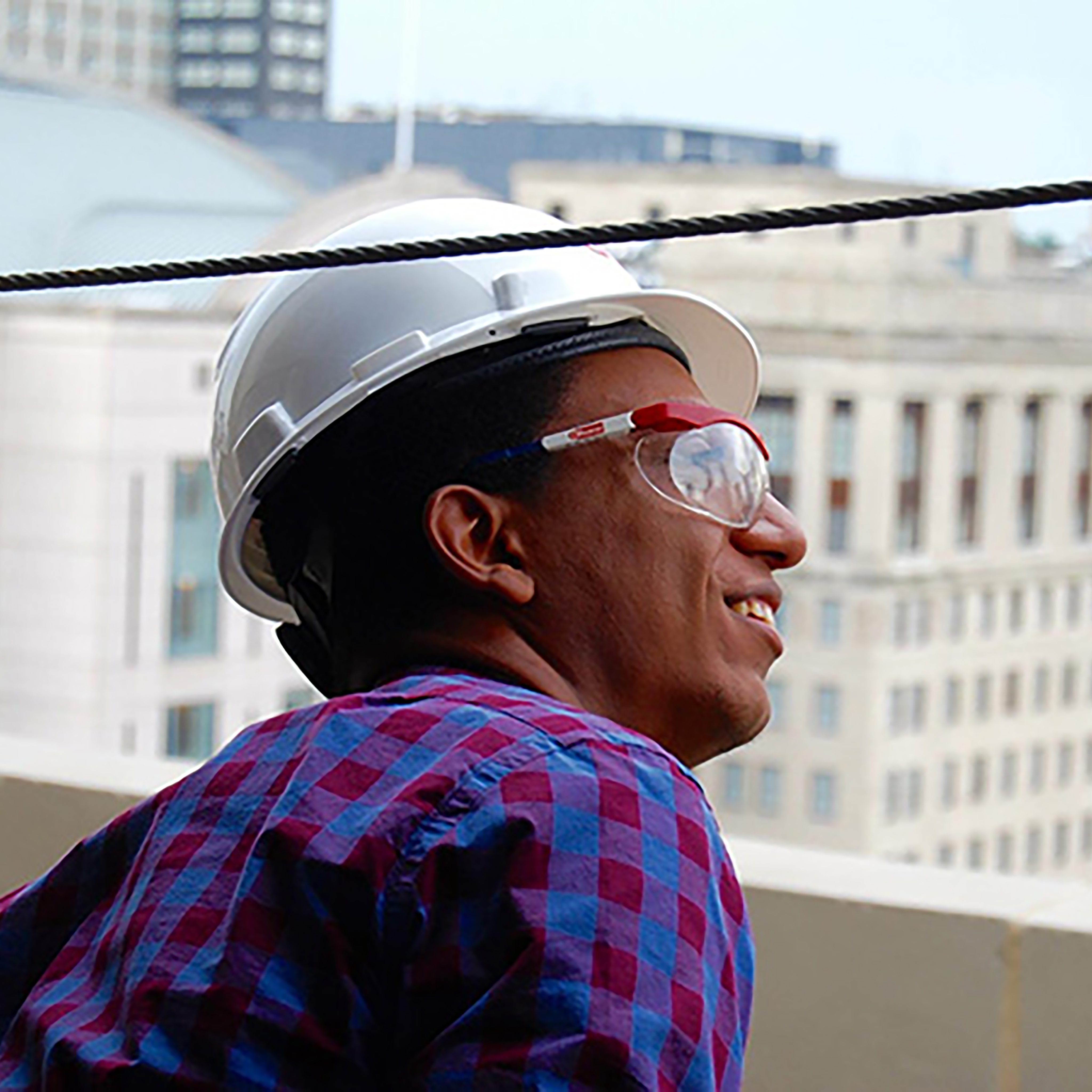 Close up photo of a man looking out of high-rise building wearing a hard hat and safety glasses.