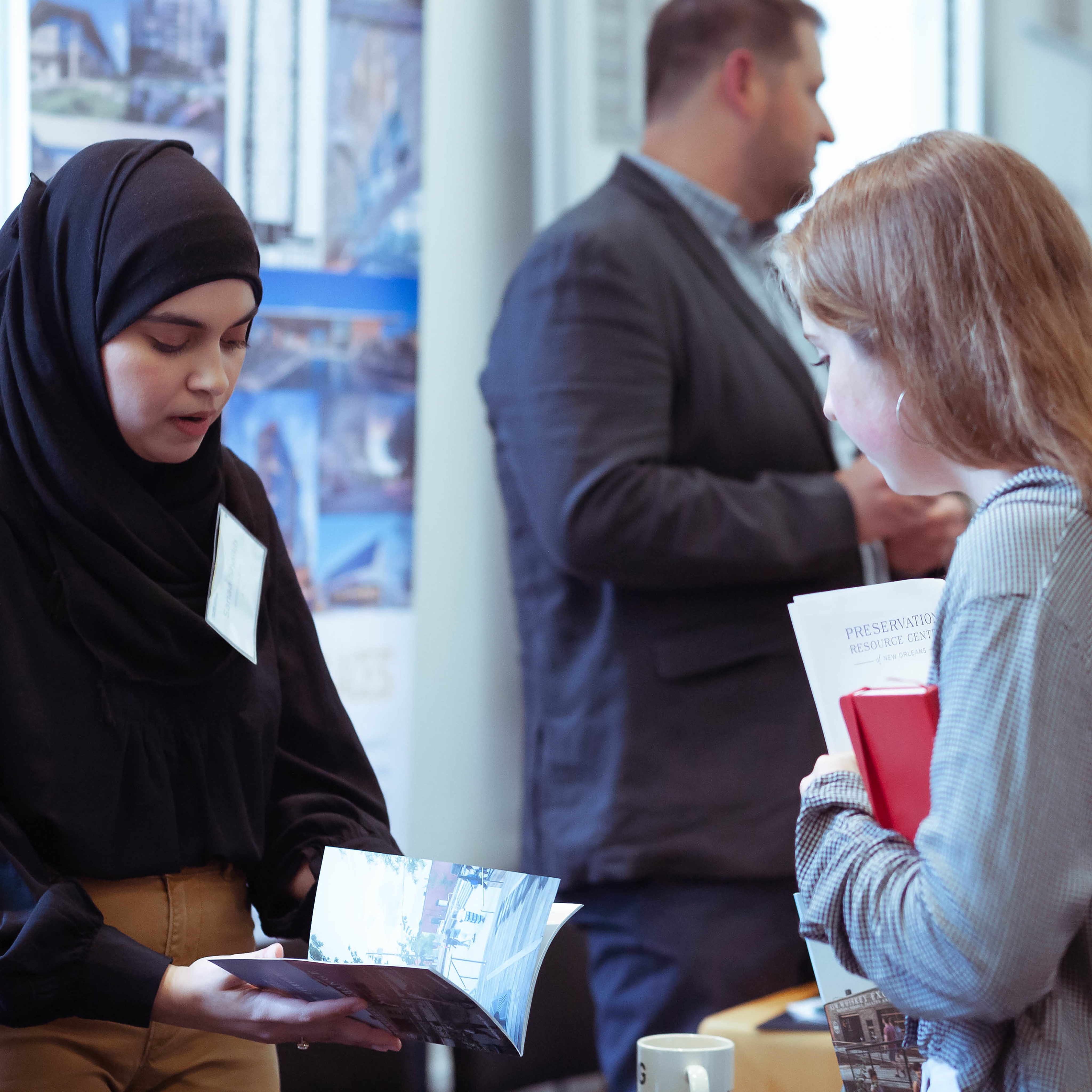 Photo from the side of two women looking down at a portfolio. The woman on the left is wearing a hijab and the woman on the right is not.