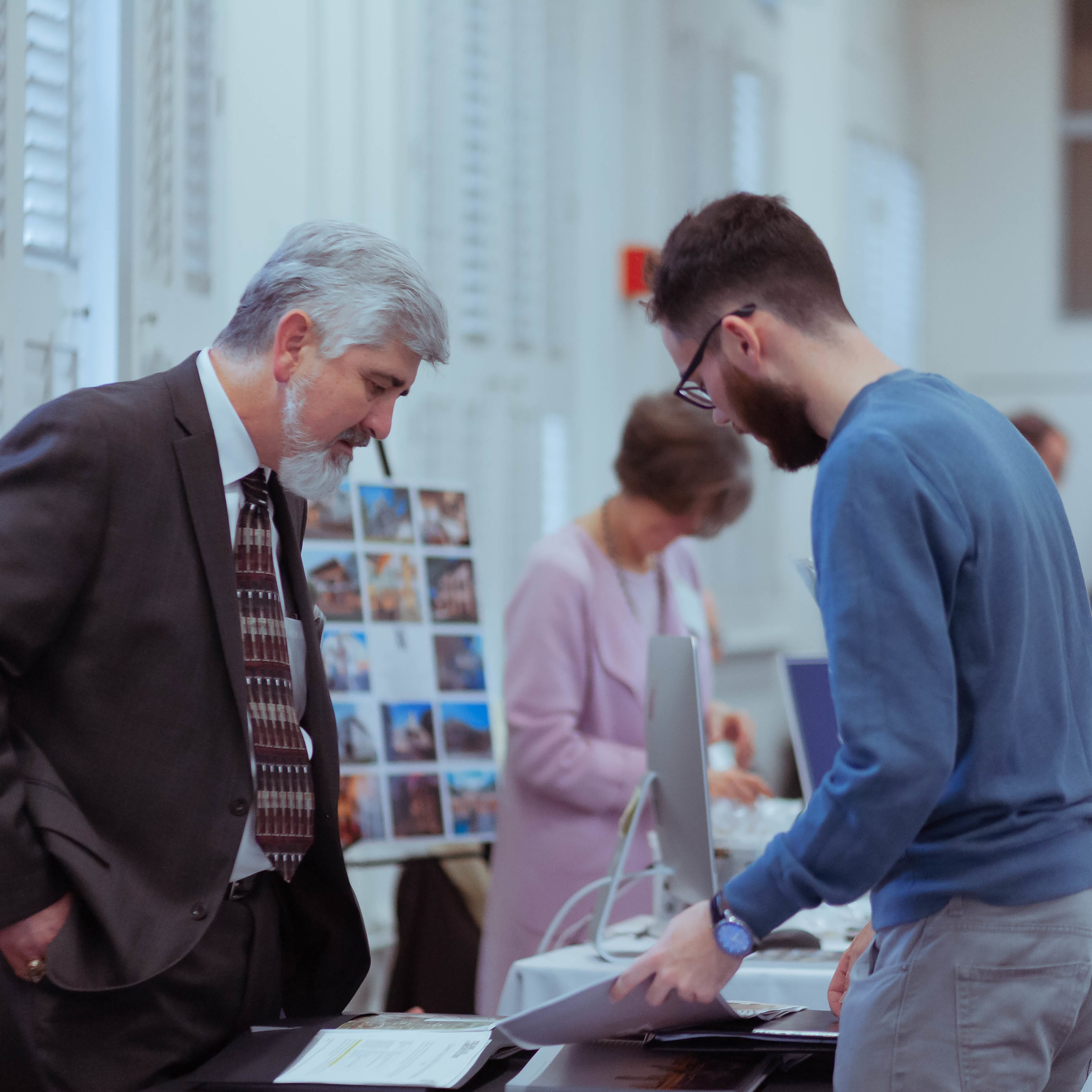 Photo from the side of two men looking down at a portfolio that the younger man on the right is holding