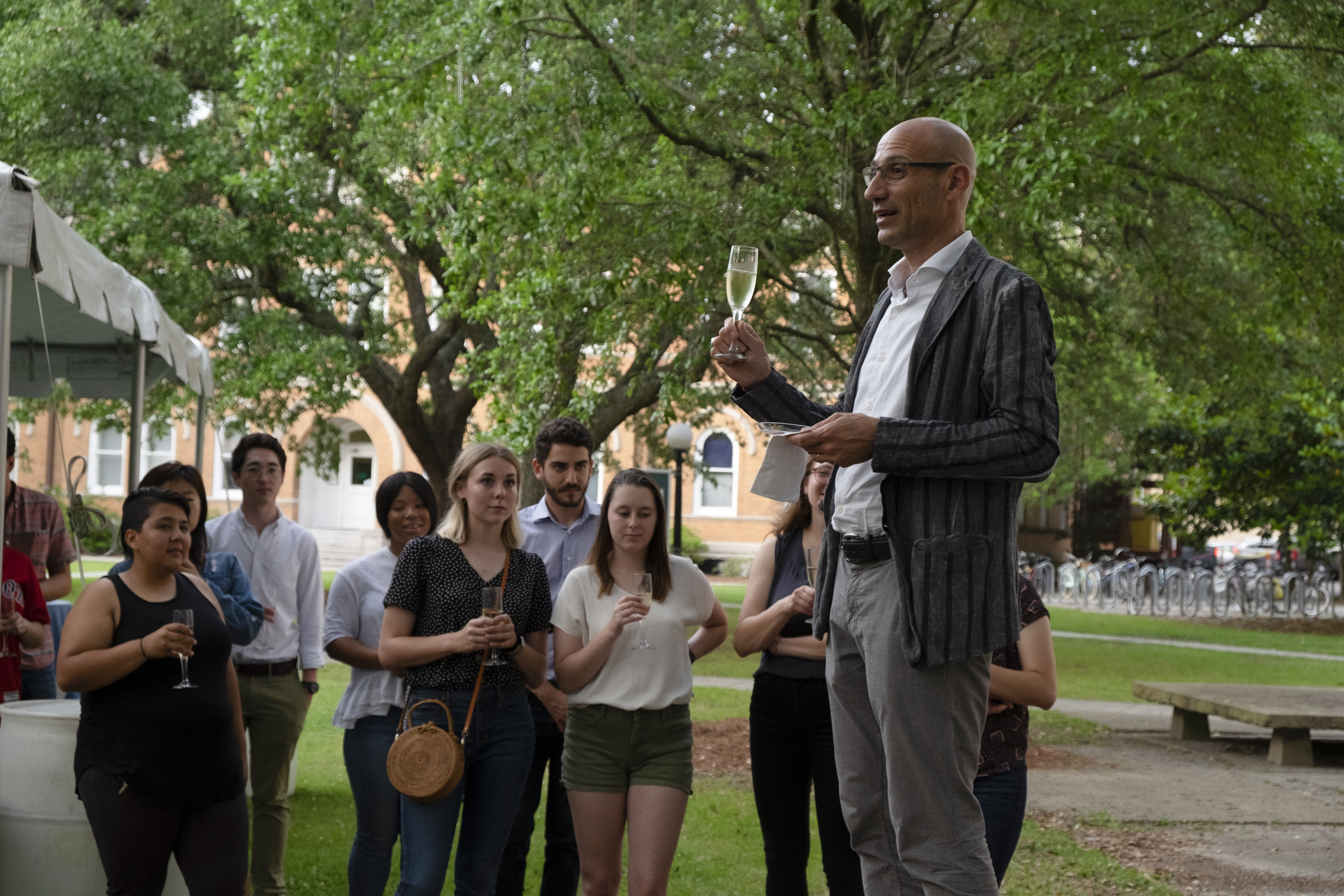 Dean Alday toasting with a glass of champagne at an outdoor reception on Tulane's campus