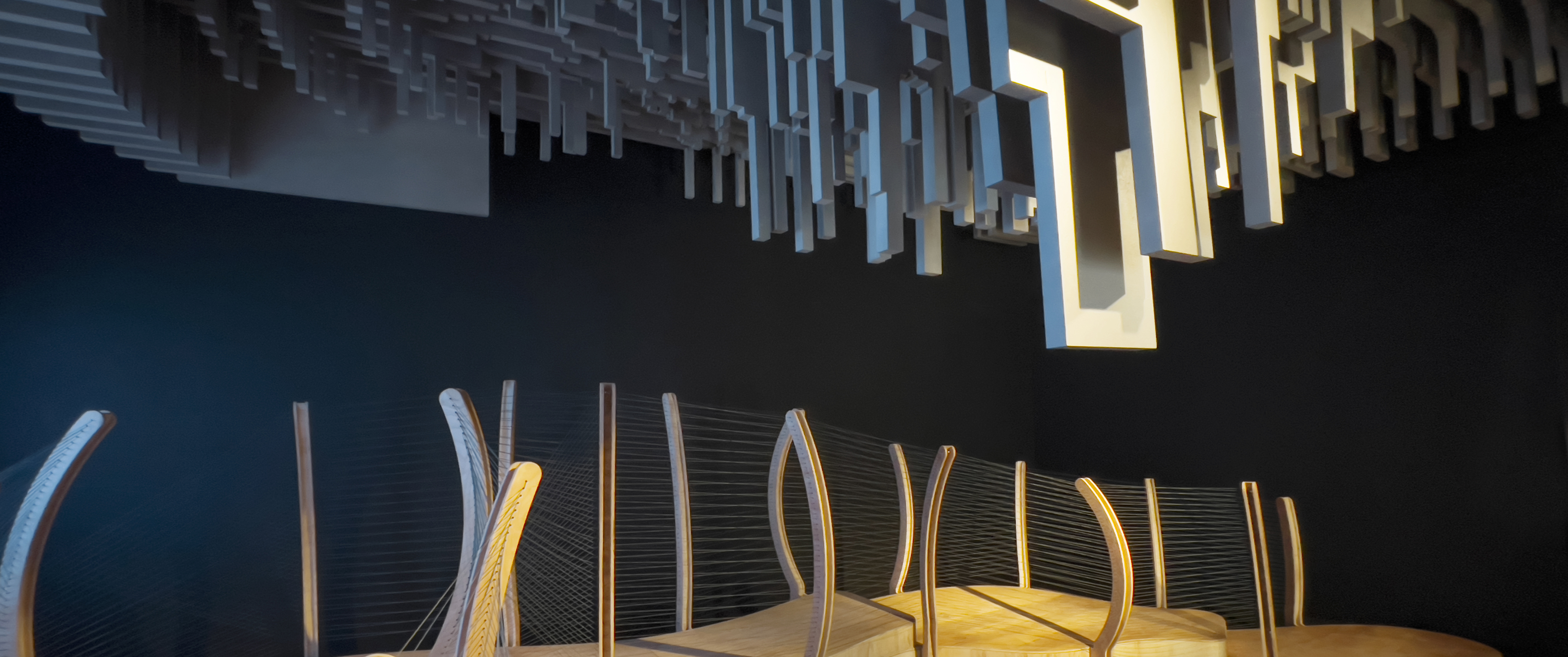 Photo inside a dark room with cut out wood panels hanging from the ceiling and a wooden walkway underneath