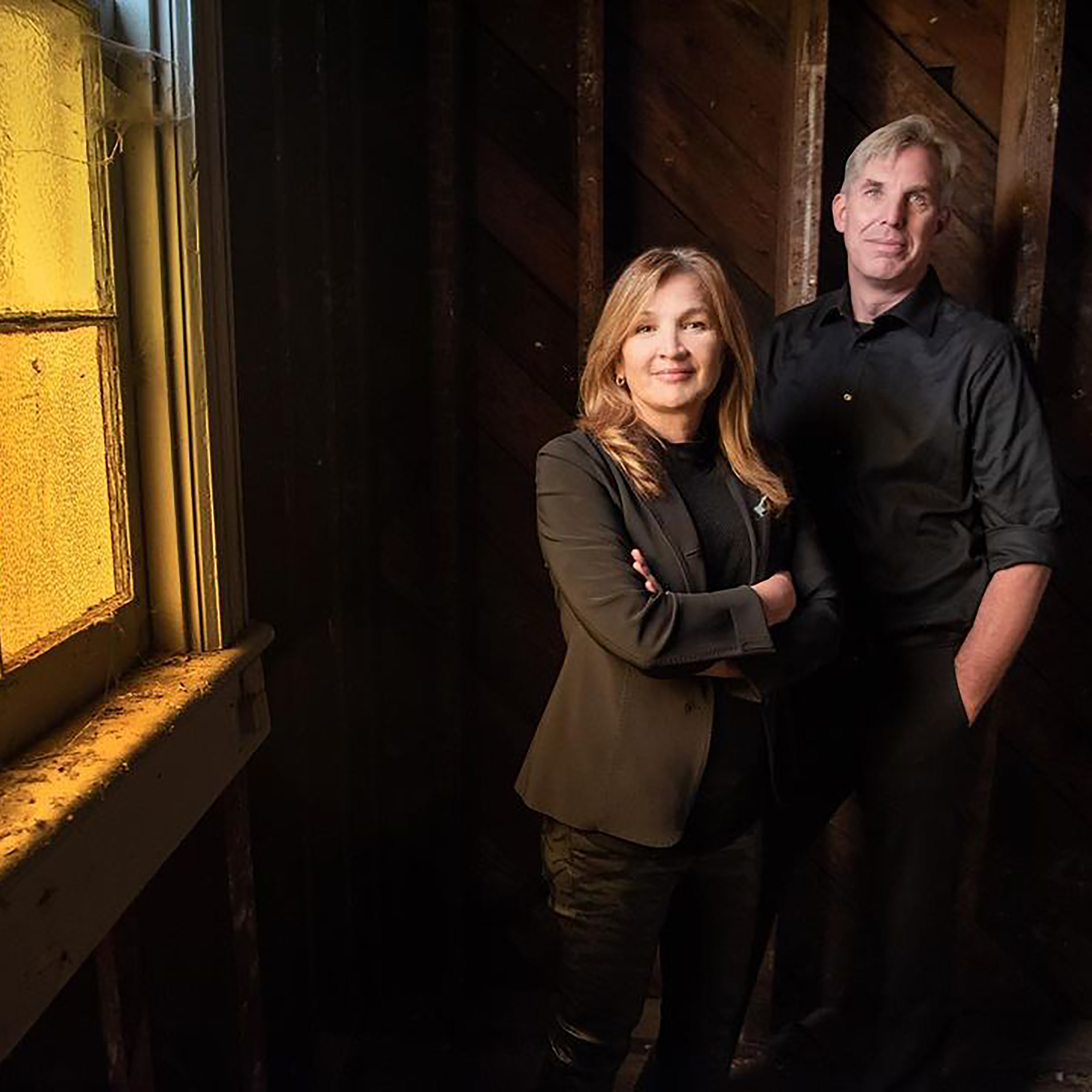 Photo of alumni Terri and Ian Dreyer standing in a dark room with a window to the left letting it a little light
