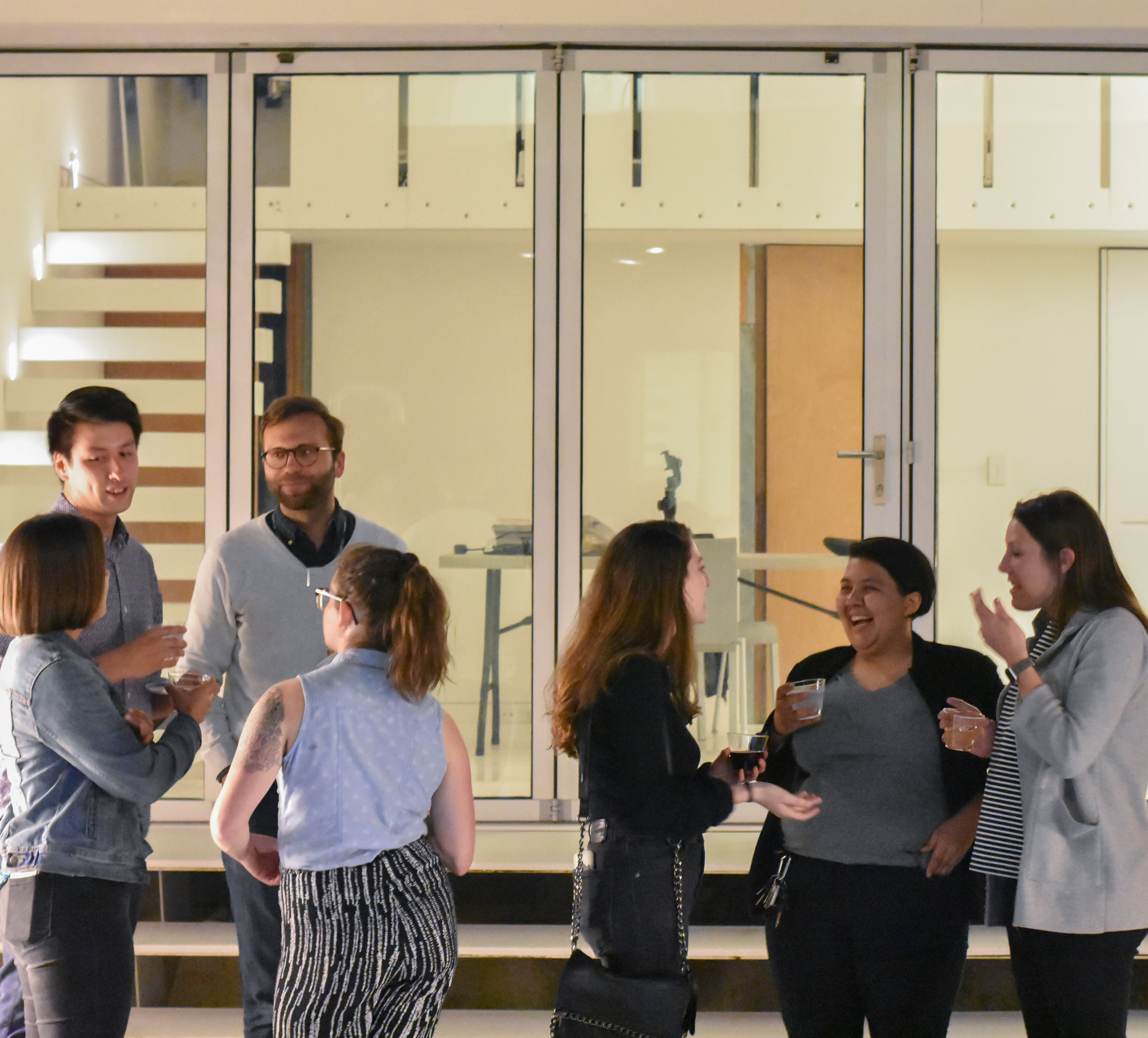 Seven students talking at an event outside of a home with glass doors