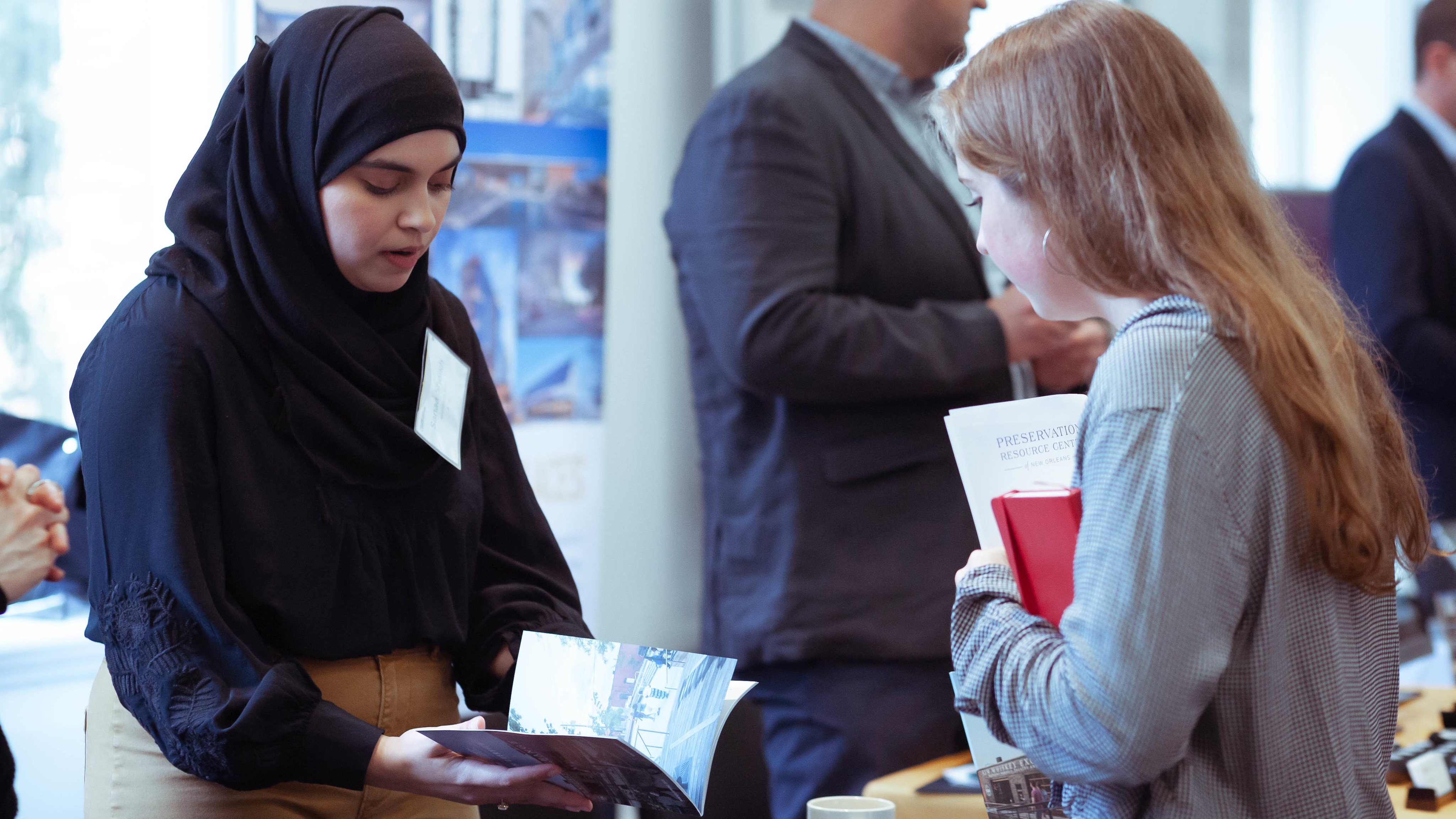 Photo of two females facing each other and looking down at a booklet one is holding.