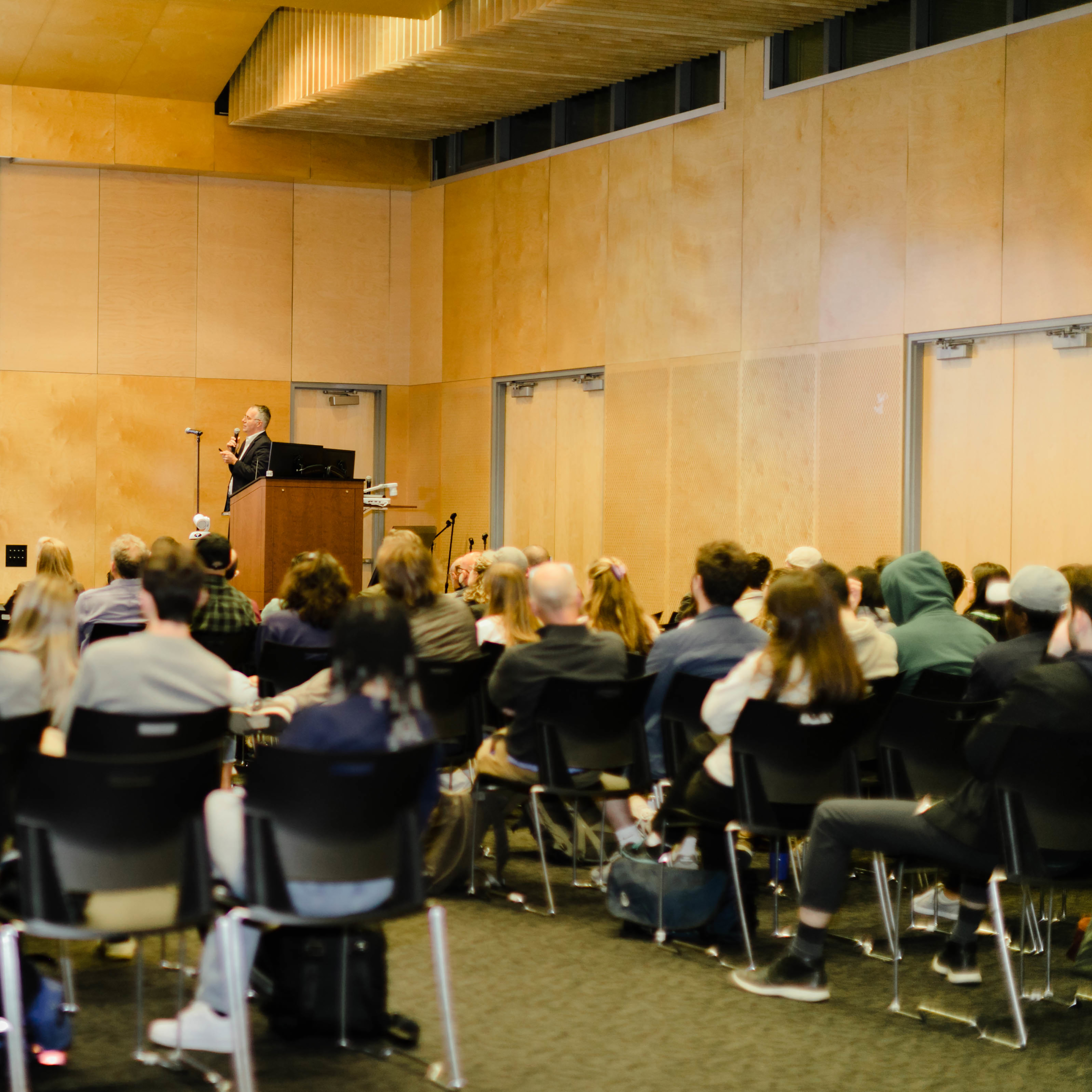 Image of students in a lecture hall watching a lecturer speak. 