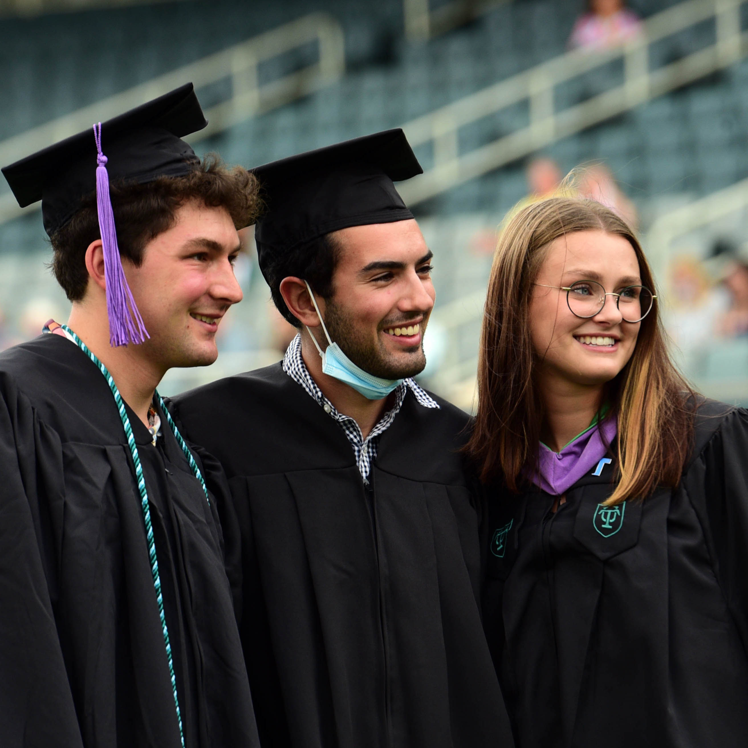 Three students in graduation robes and hats, pose and smile looking off camera to the right for a photo.