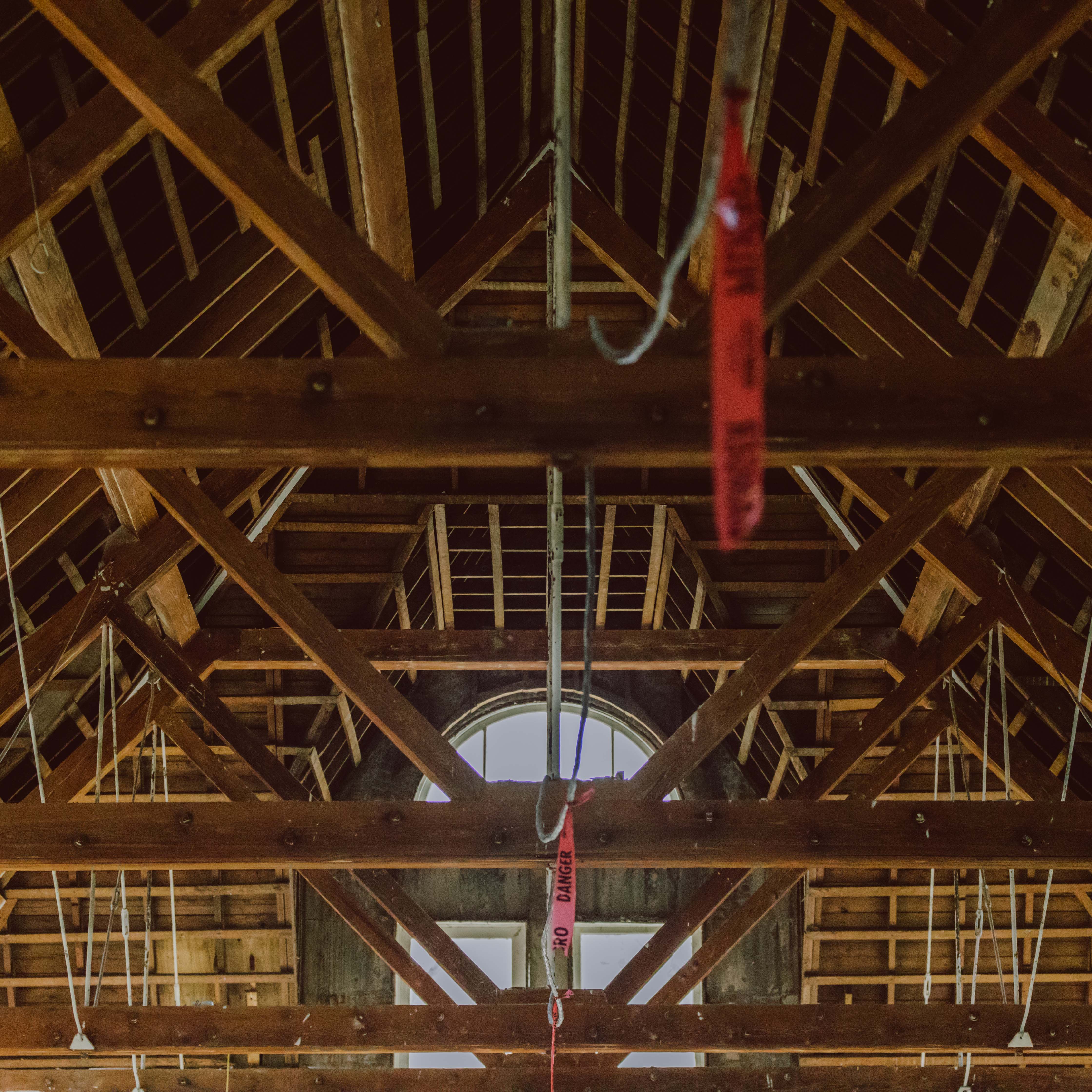 Interview photo looking up at exposed wooden trusses and roof structure at historic renovation site. 