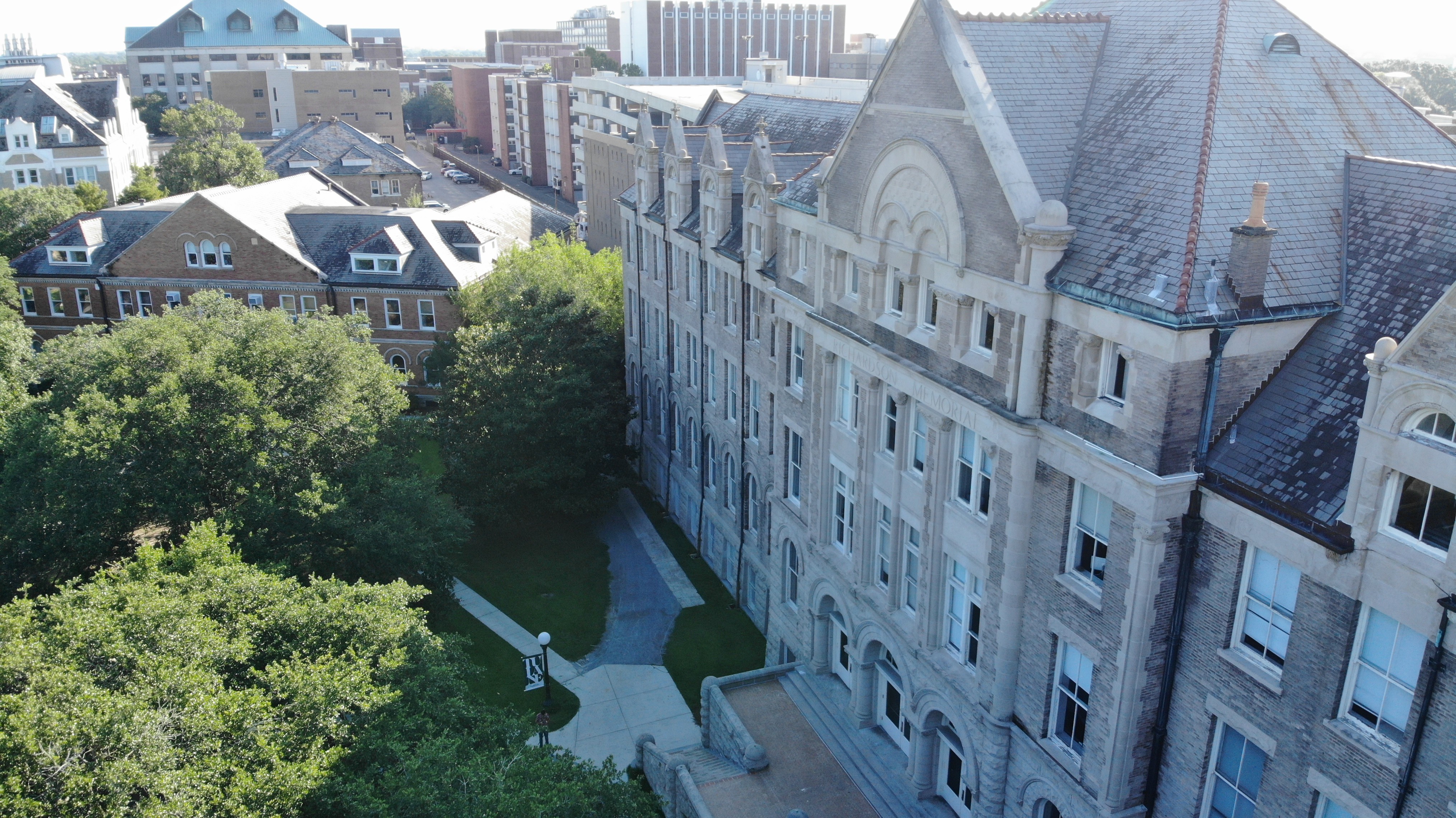 Aerial photo overlooking an academic quad with lush trees and a historic 5-story building, featuring a Romanesque brick and limestone façade