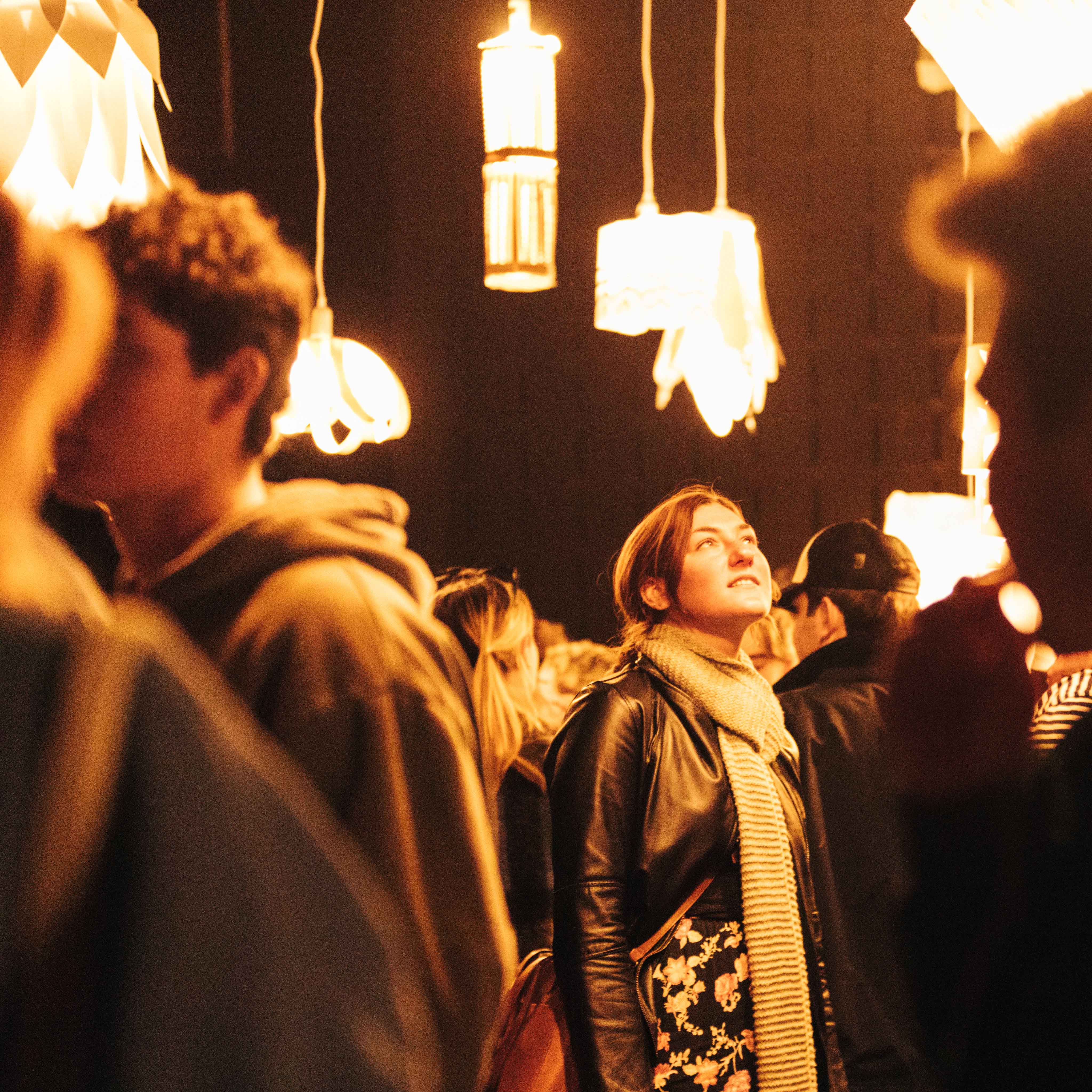 Inside view of a darkened room and lots of people looking up at bright light fixtures created by students hanging on individual power cords