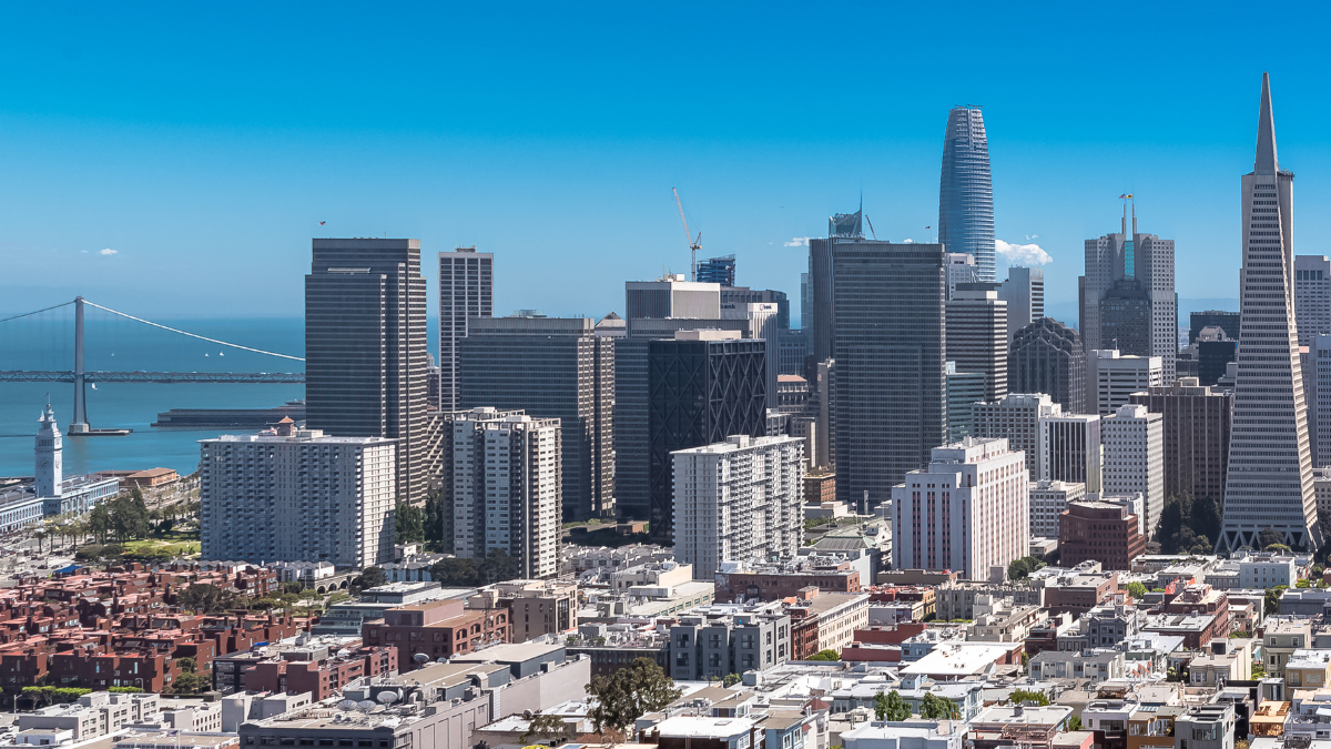 Aerial photo of the skyline of San Francisco with the Golden Gate bridge in the far left distance and towers in the middle and far right distance and smaller residences and buildings in the foreground.
