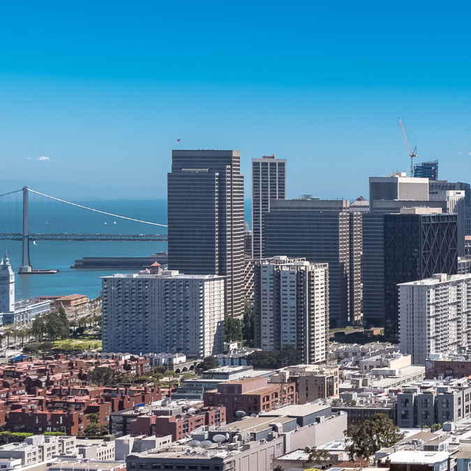 Aerial photo of the skyline of San Francisco with the Golden Gate bridge in the far left distance and towers in the middle and far right distance and smaller residences and buildings in the foreground.