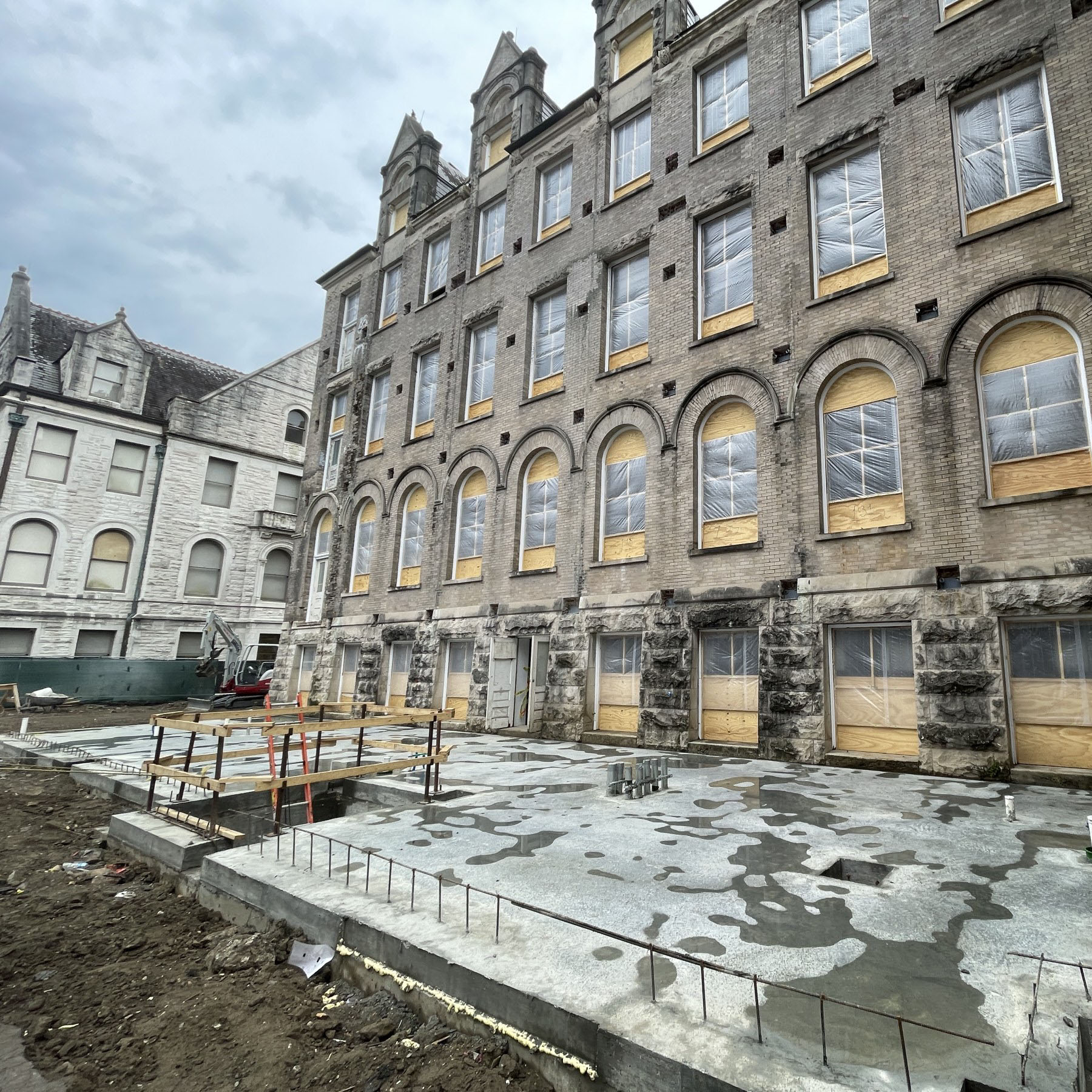 View from the back of a historic limestone building with new slab in foreground, showing that the building will be getting an addition built onto it.