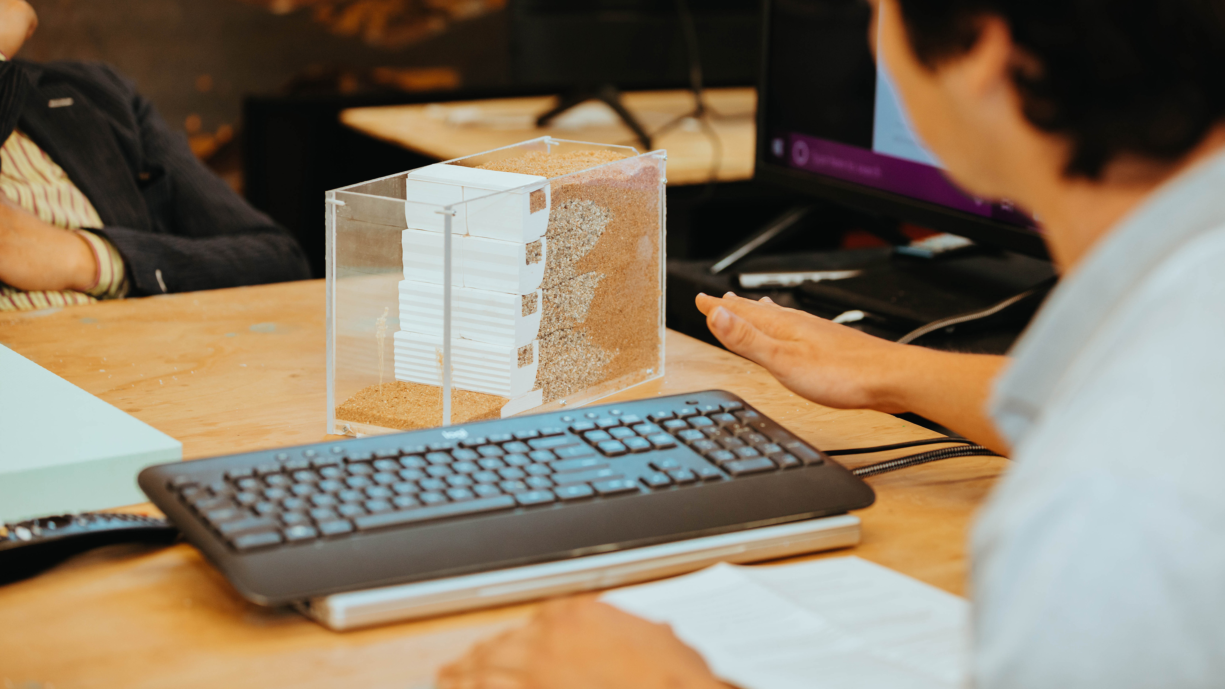Close up of a hydrological model on a students desk with the students hands and arms in the frame, along with the students' computer keyboard.