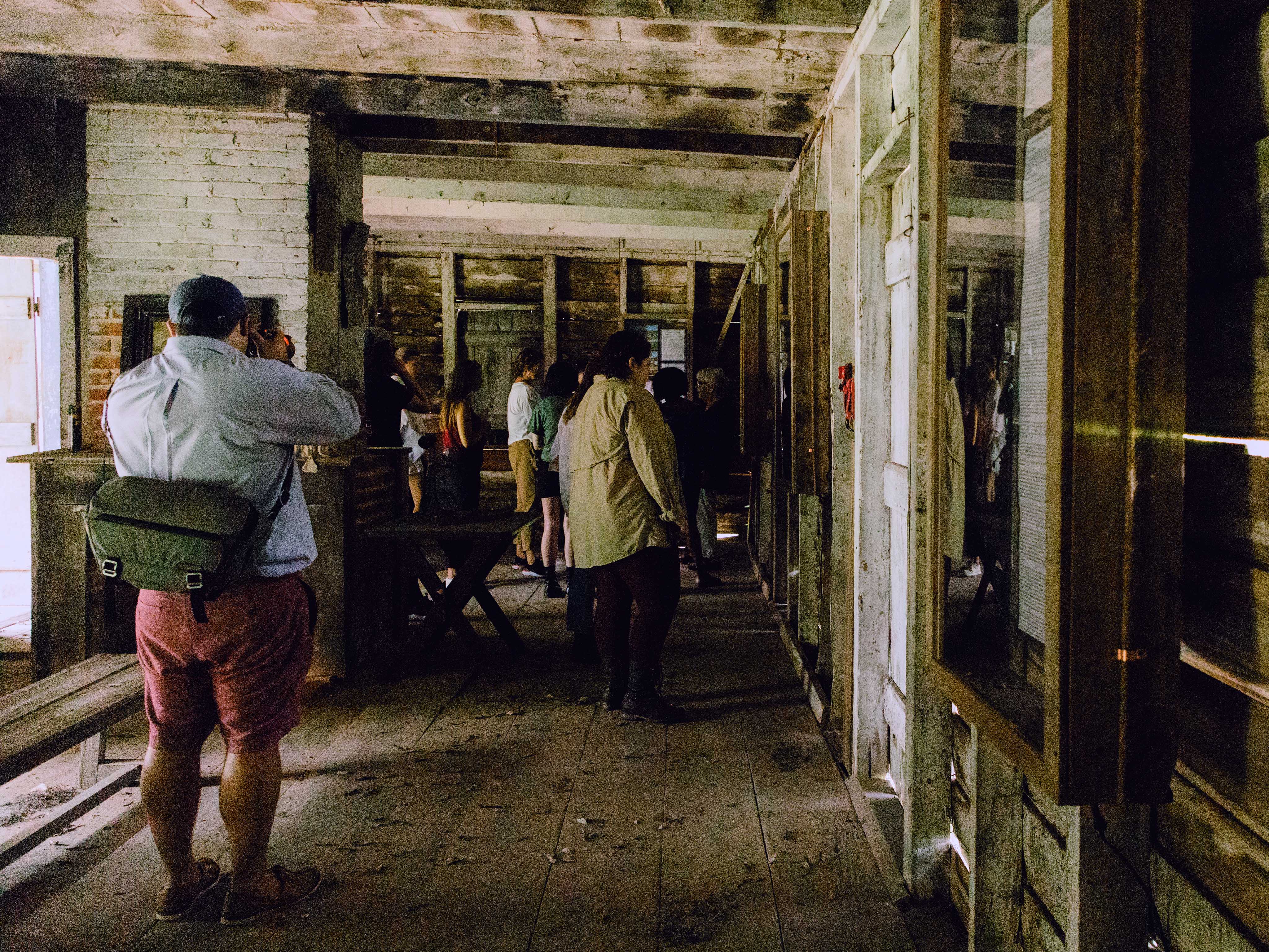 Interior of a historic wooden cottage with exposed interior walls and beams, with student walking in the background.