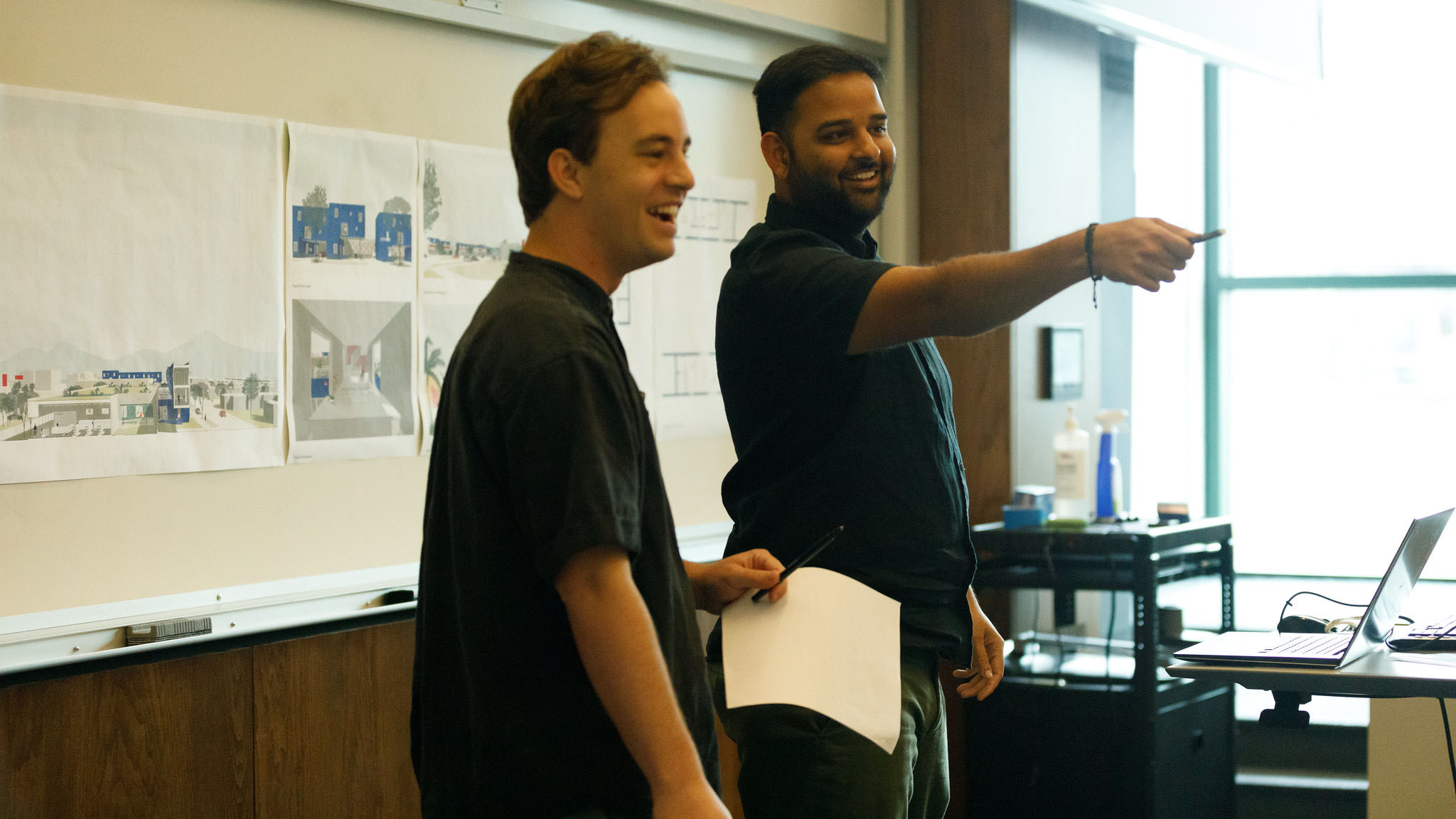 a professor and student stand next to each other, reviewing the students thesis project