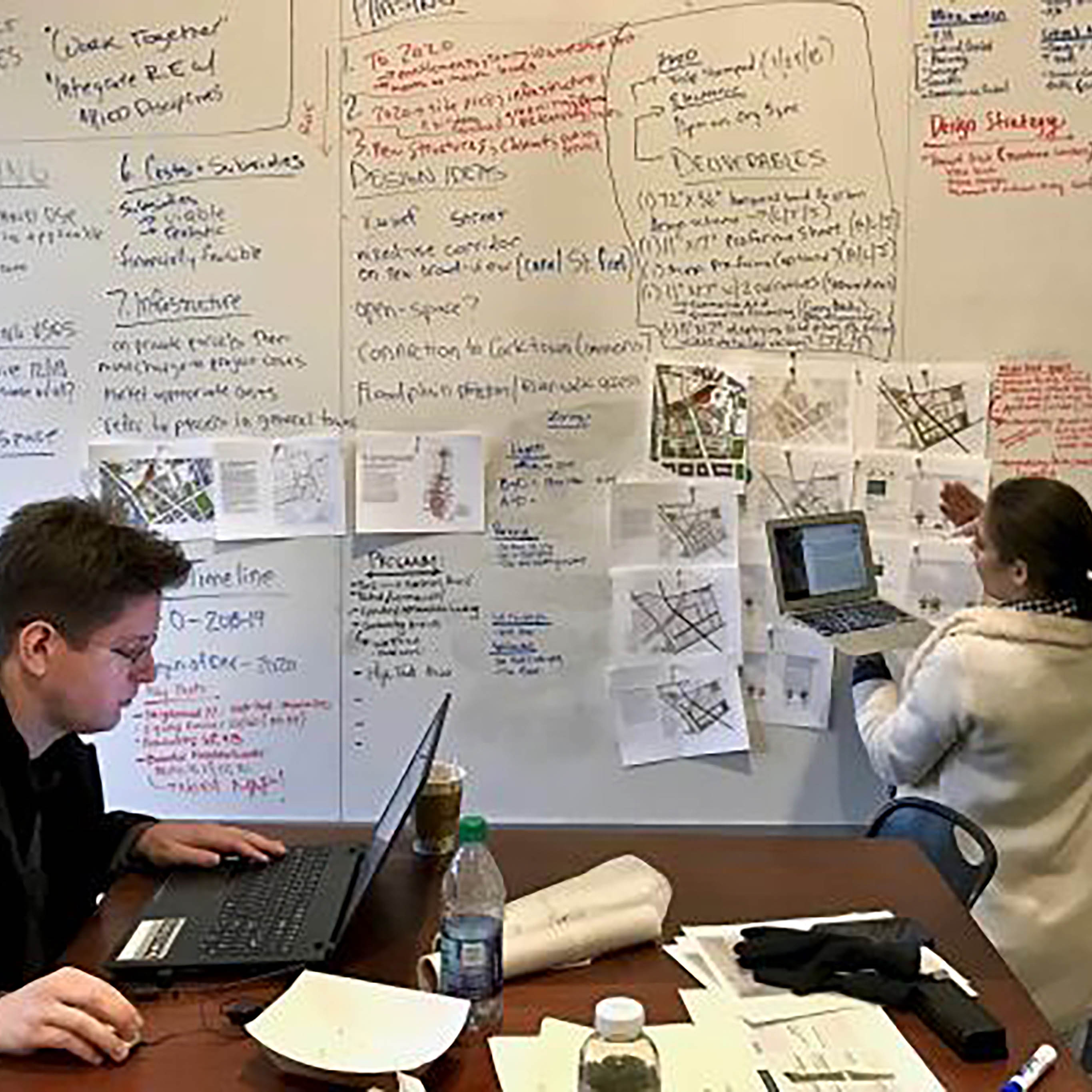 Three students working collaboratively on computers and writing on whiteboard