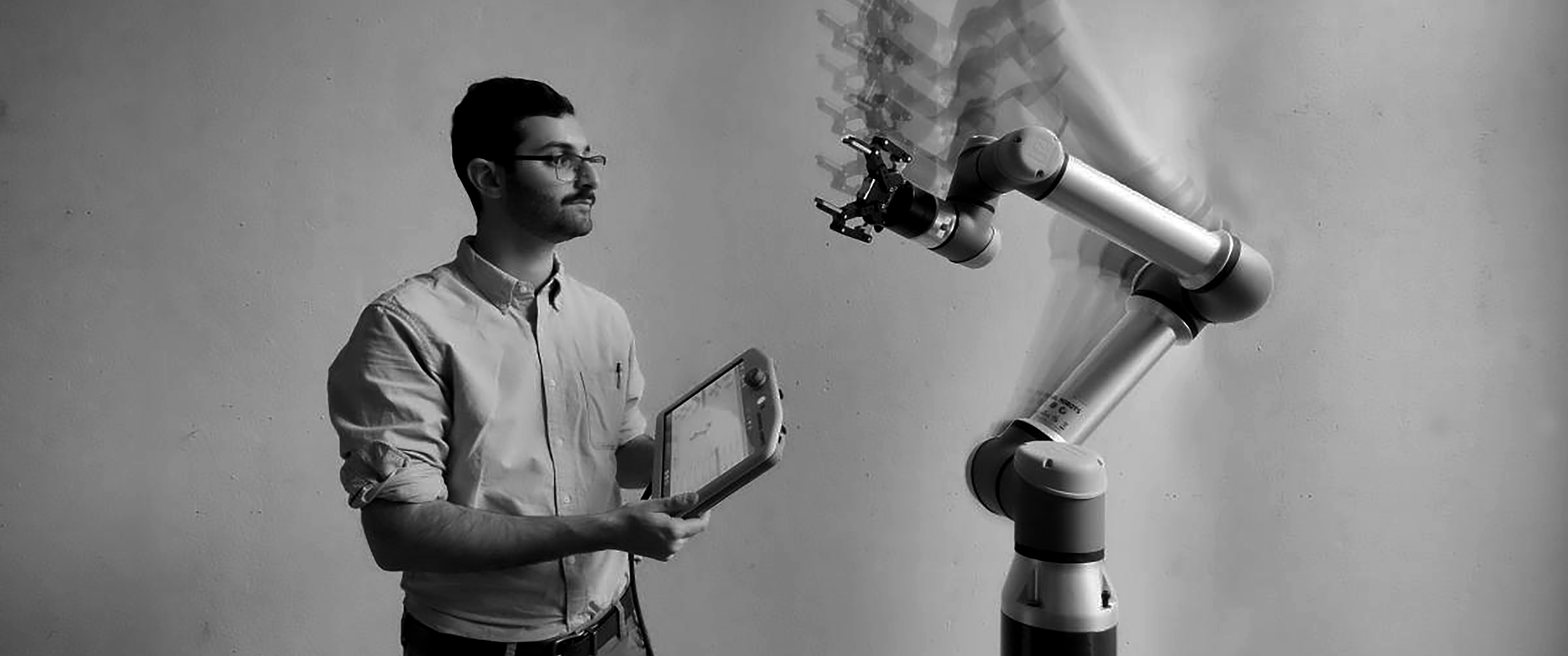 Man standing on left of the frame looking at a robot arm moving on the right of the frame.