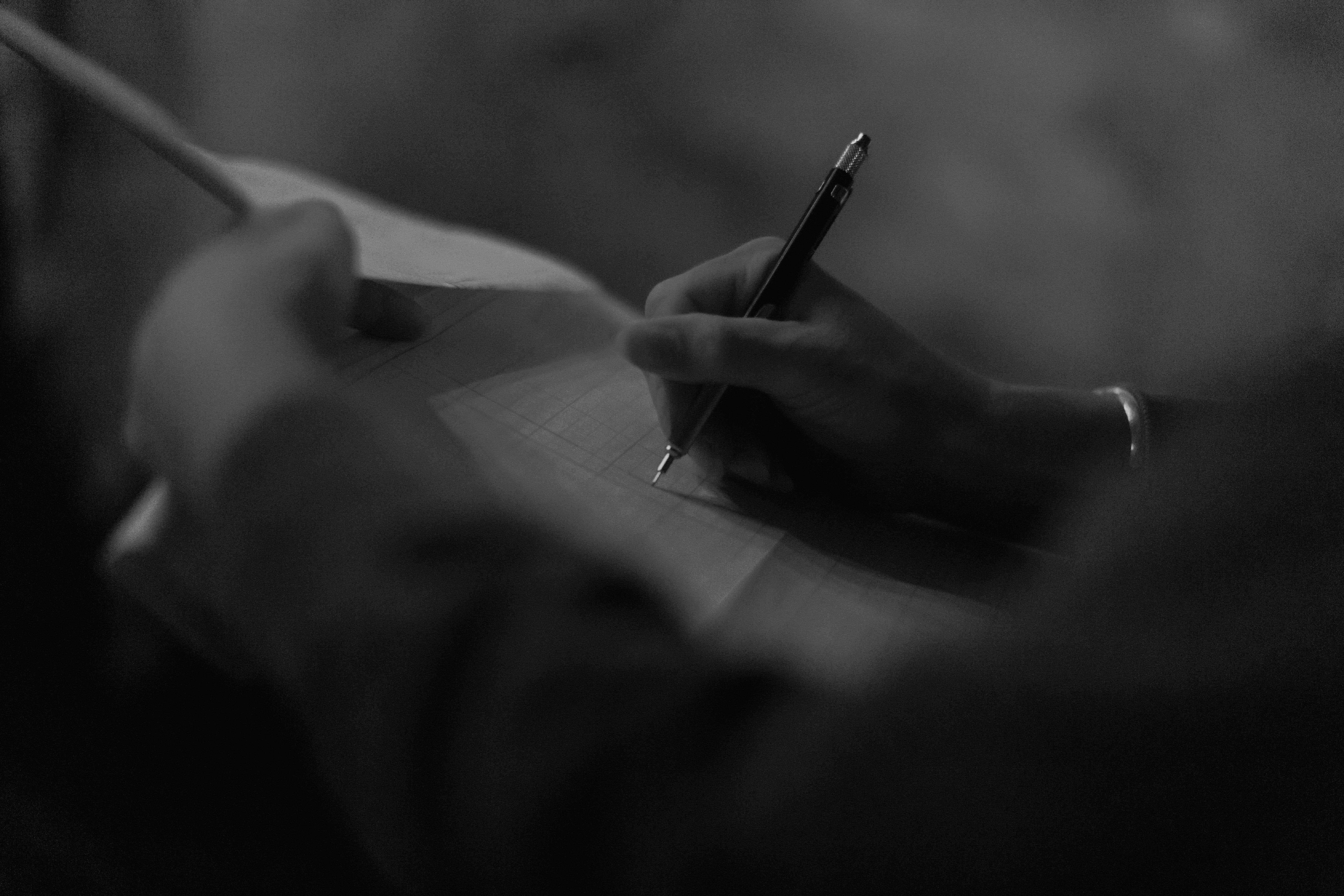 Close up of a hand with a pen writing on paper in a darkened room.