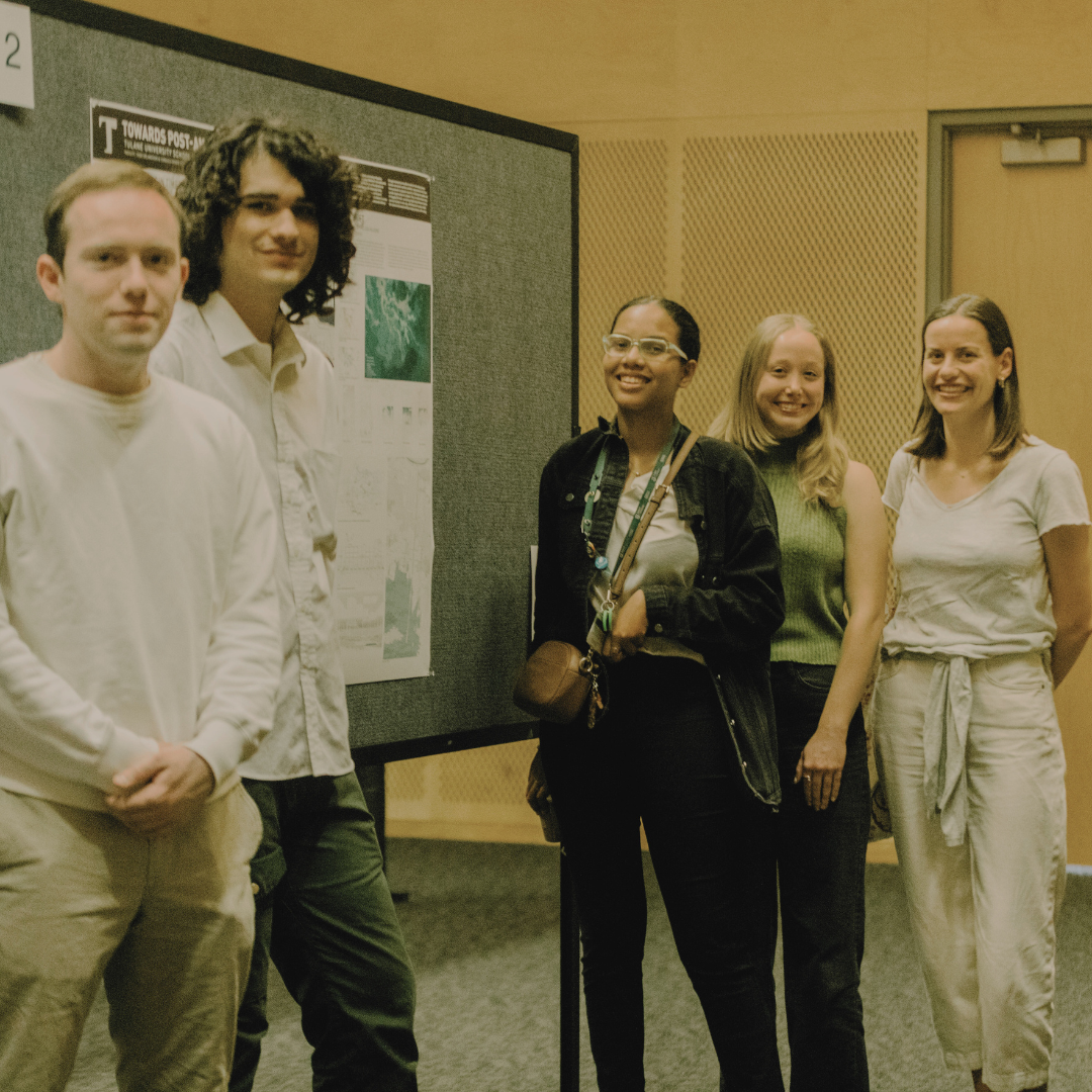 Five students stand and smile next to to a poster presentation on their thesis projects.