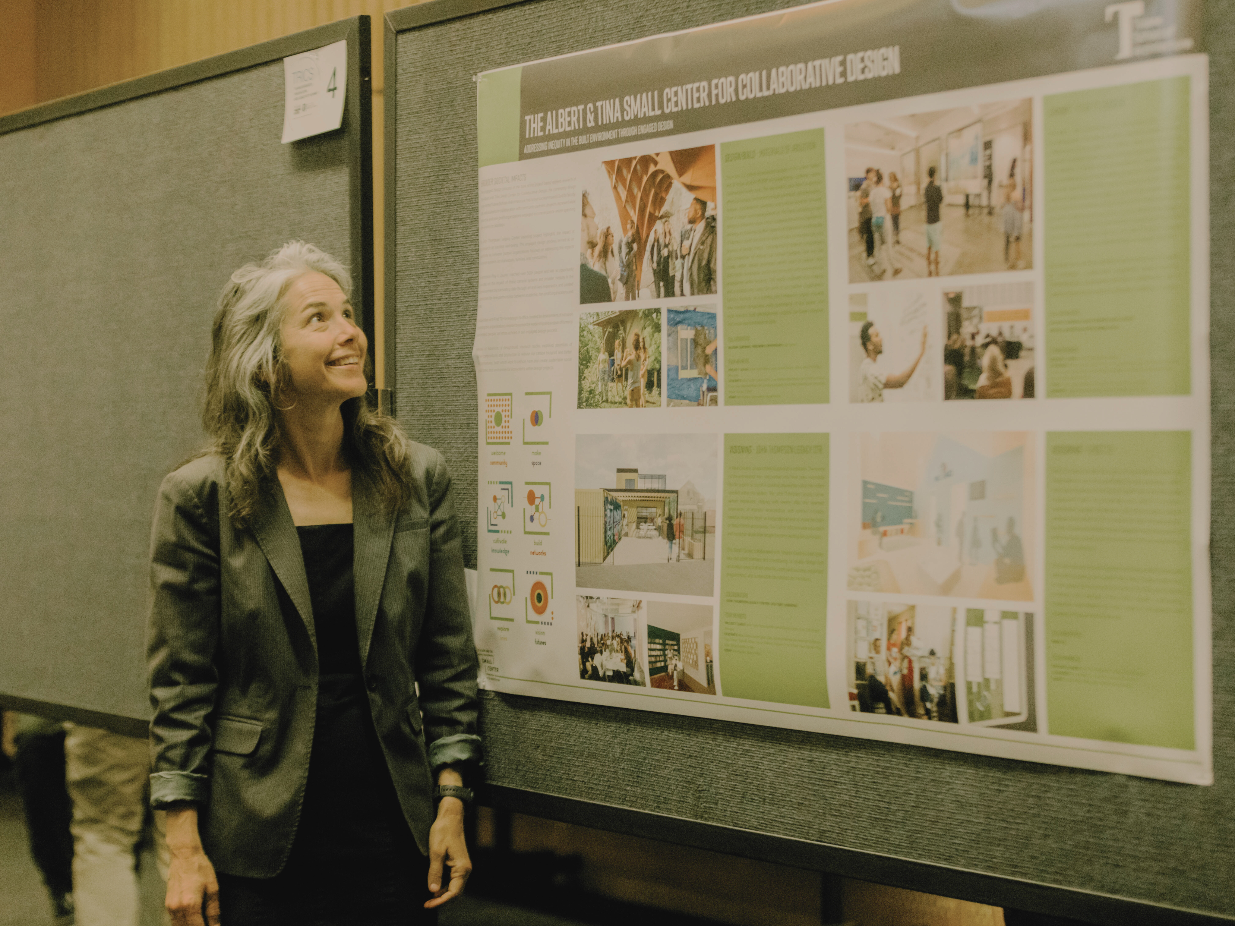 Faculty and Small Center Director Ann Yoachim stands next to a large poster that describes the work of the Small Center as Tulane's community-engaged design center.