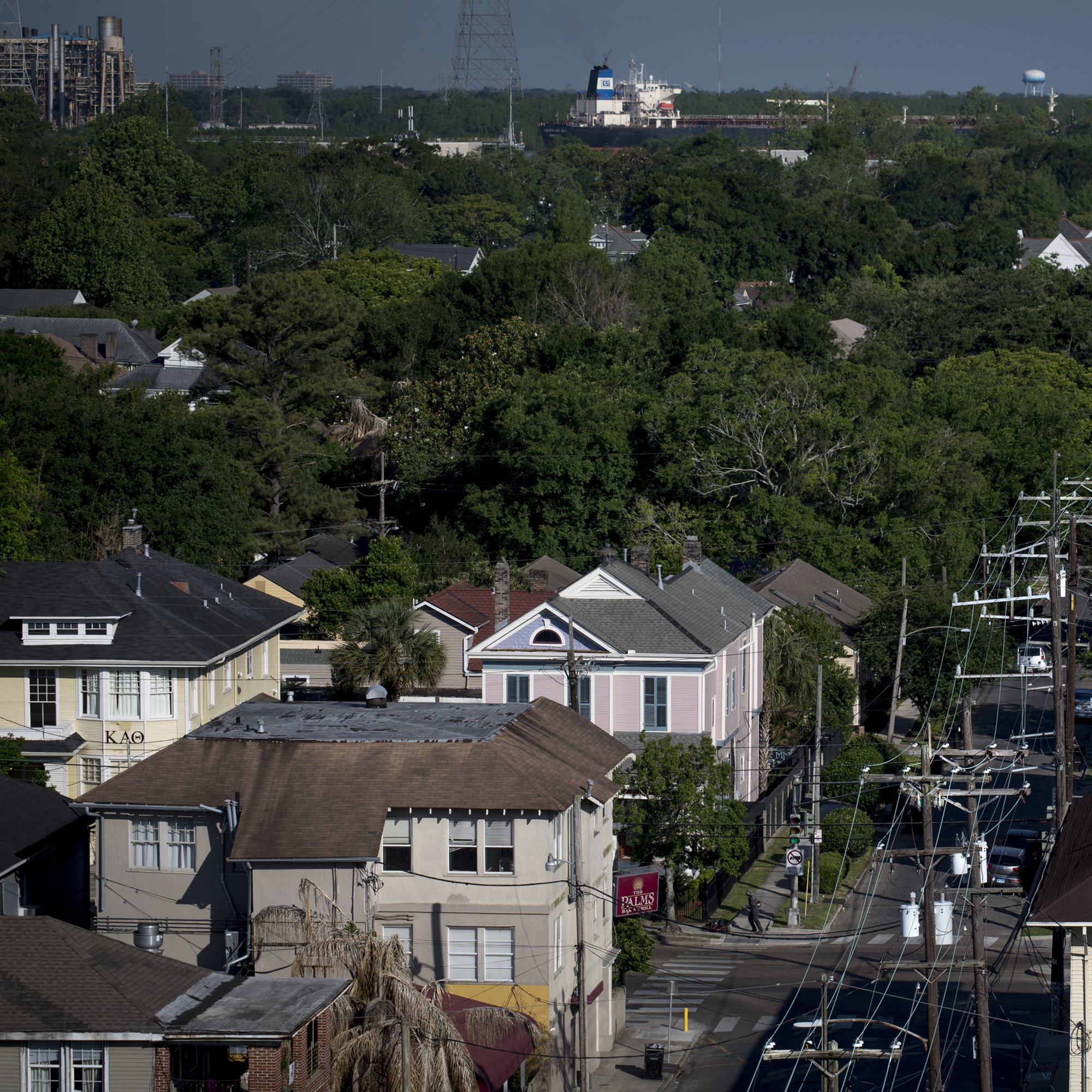 Aerial view New Orleans city street with homes and power lines in foreground and mix of trees and industrial facilities in background.