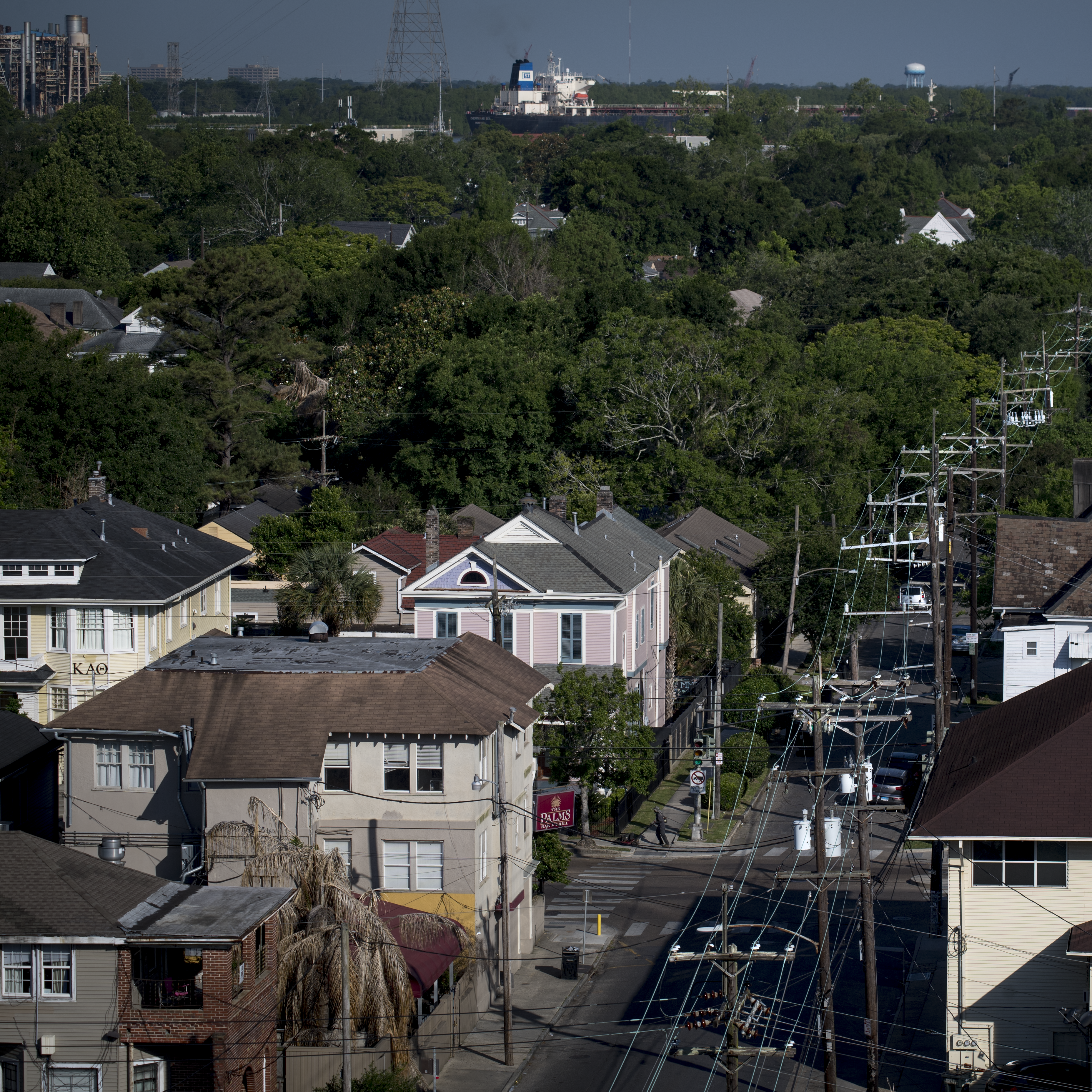 Aerial view of a New Orleans city street with power lines overhead and a mix of trees and industrial facilities in the background.