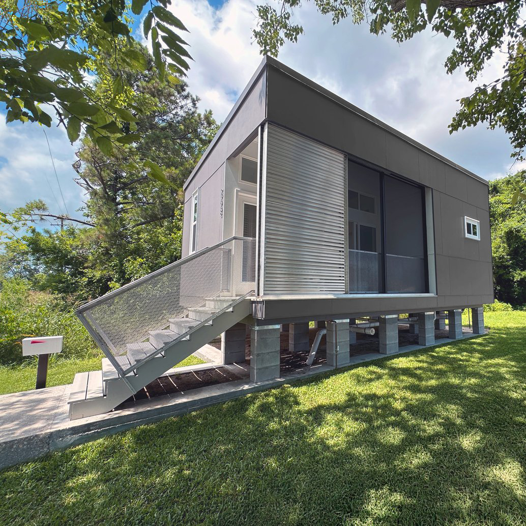 small grey square house on stilts with long glass panels