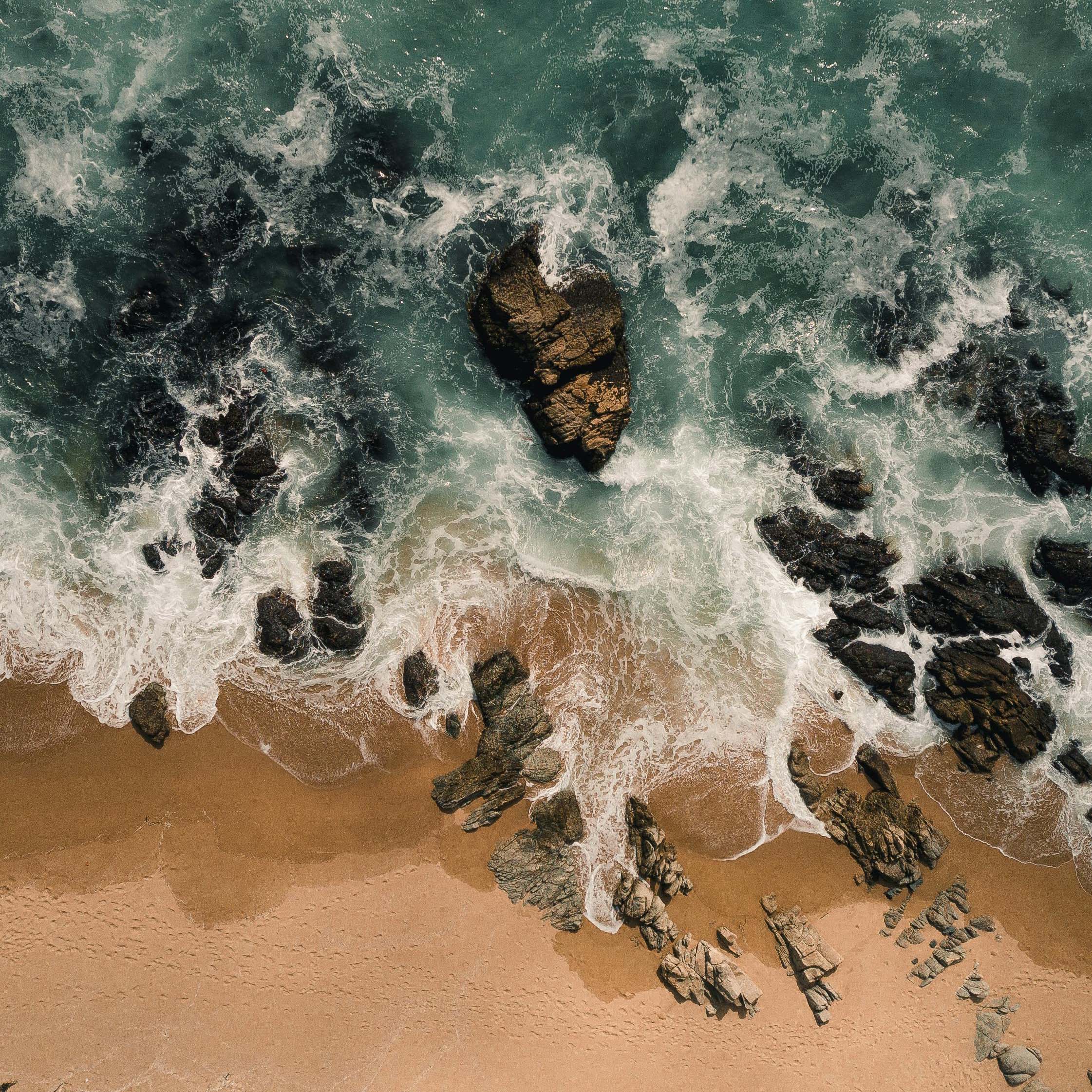Aerial view of a beach with waves on rocks and sand.
