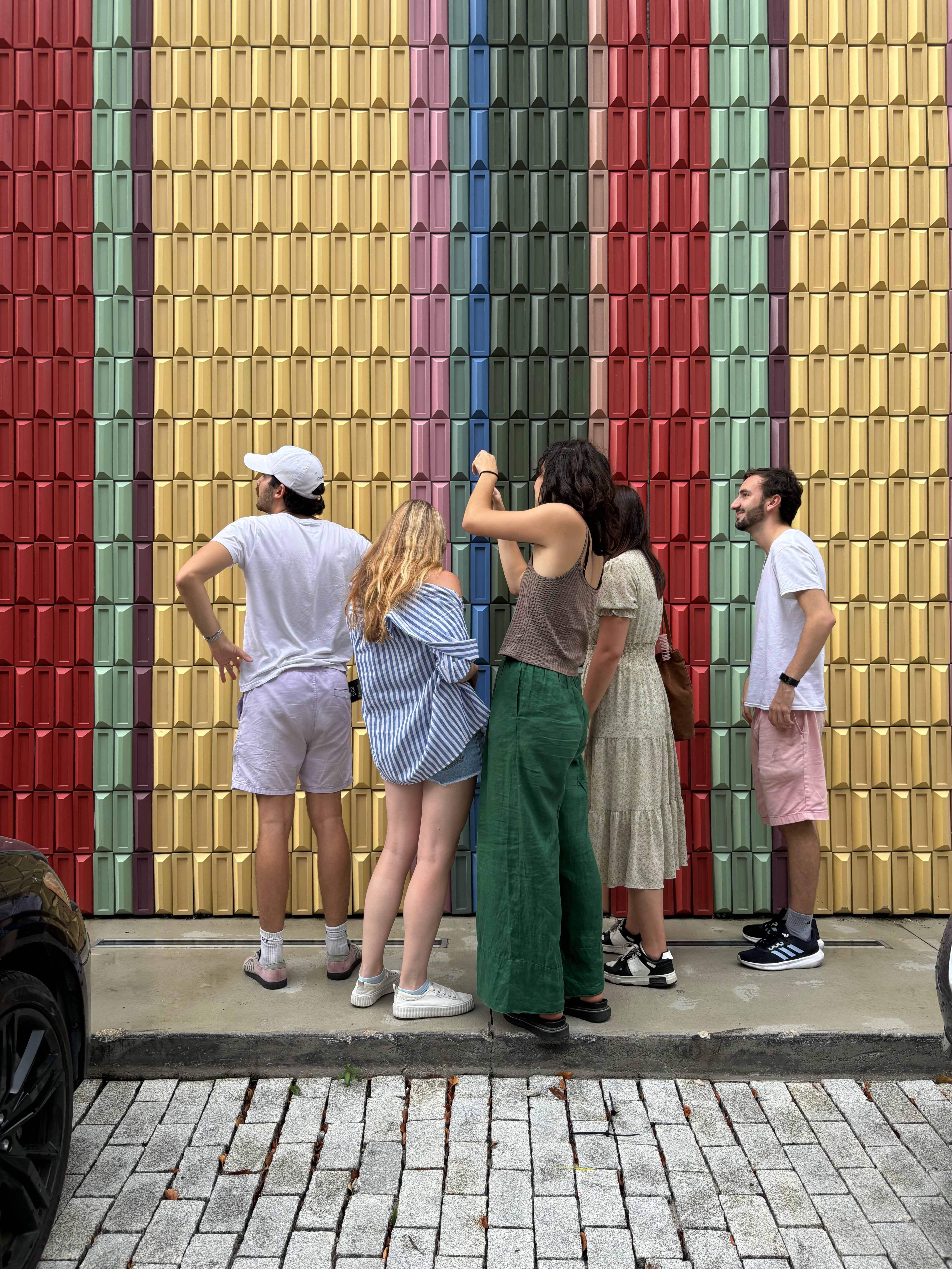 Photo os students standing on a sidewalk in front of a patterned, textured wall, for a research studio field trip.