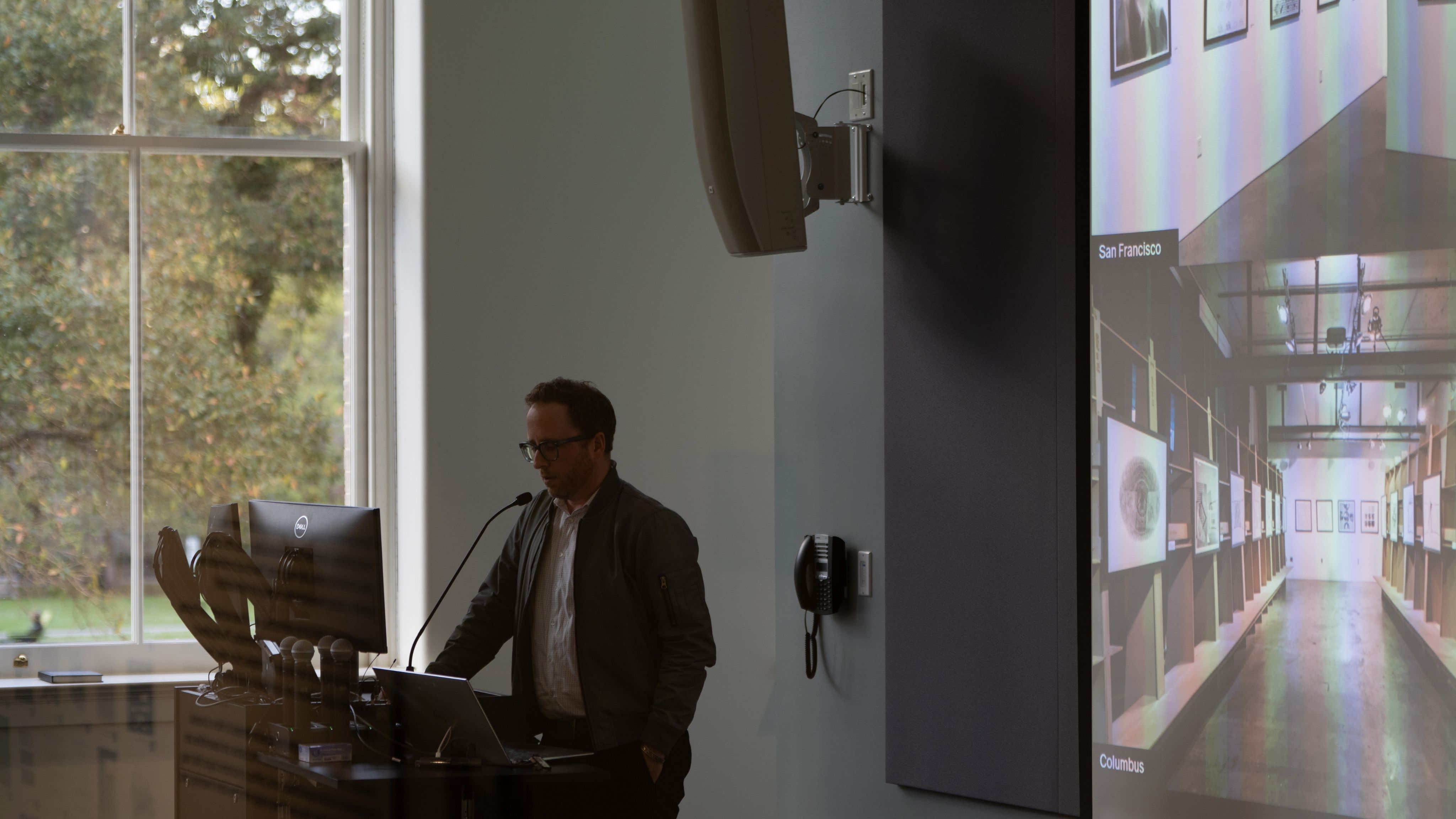 Angled view of a faculty presenting at a podium in front of a projector screen.