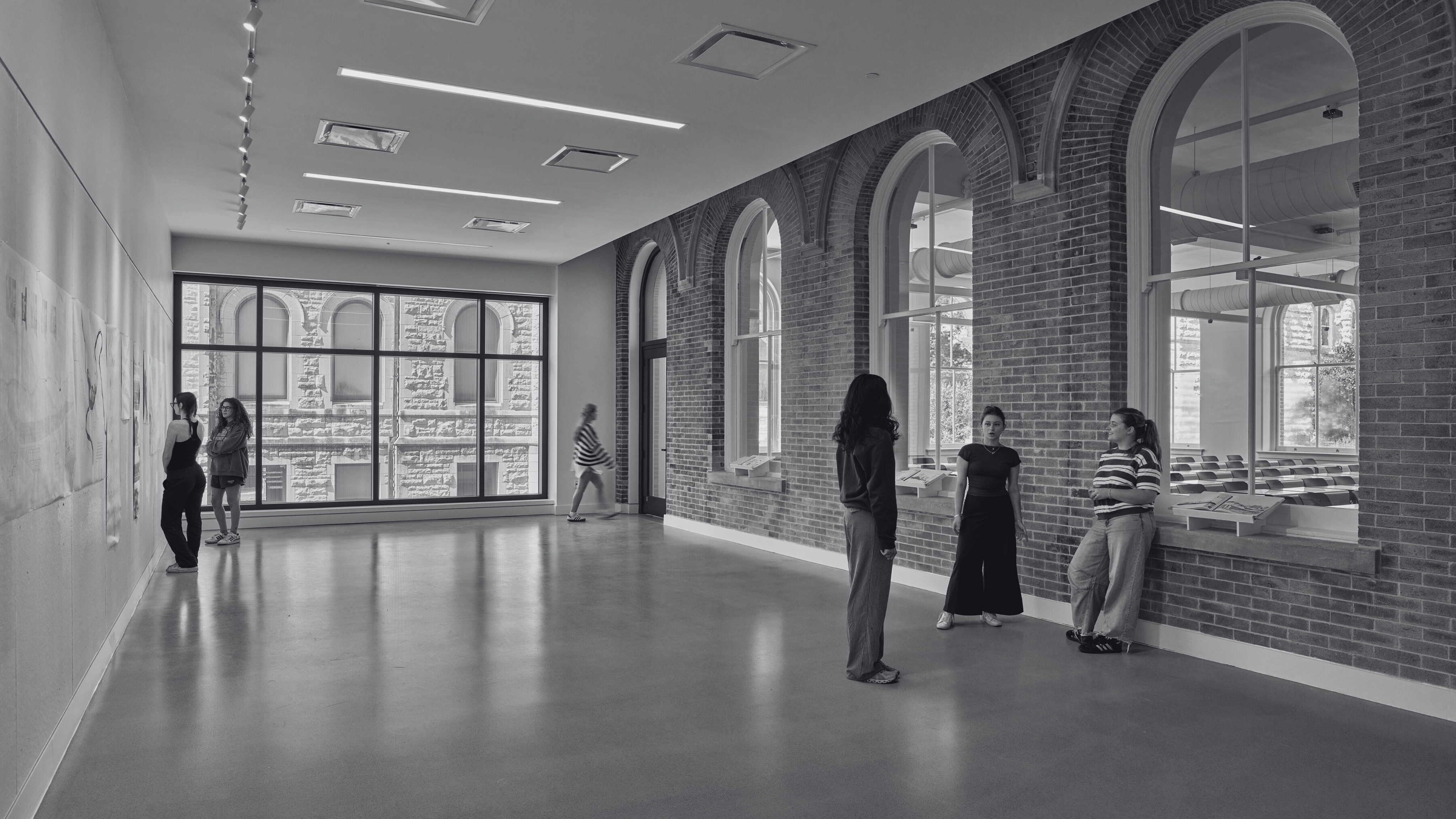 Inside view of empty Gallery room with six students standing, talking, and looking at pinned up drawings around the room. 