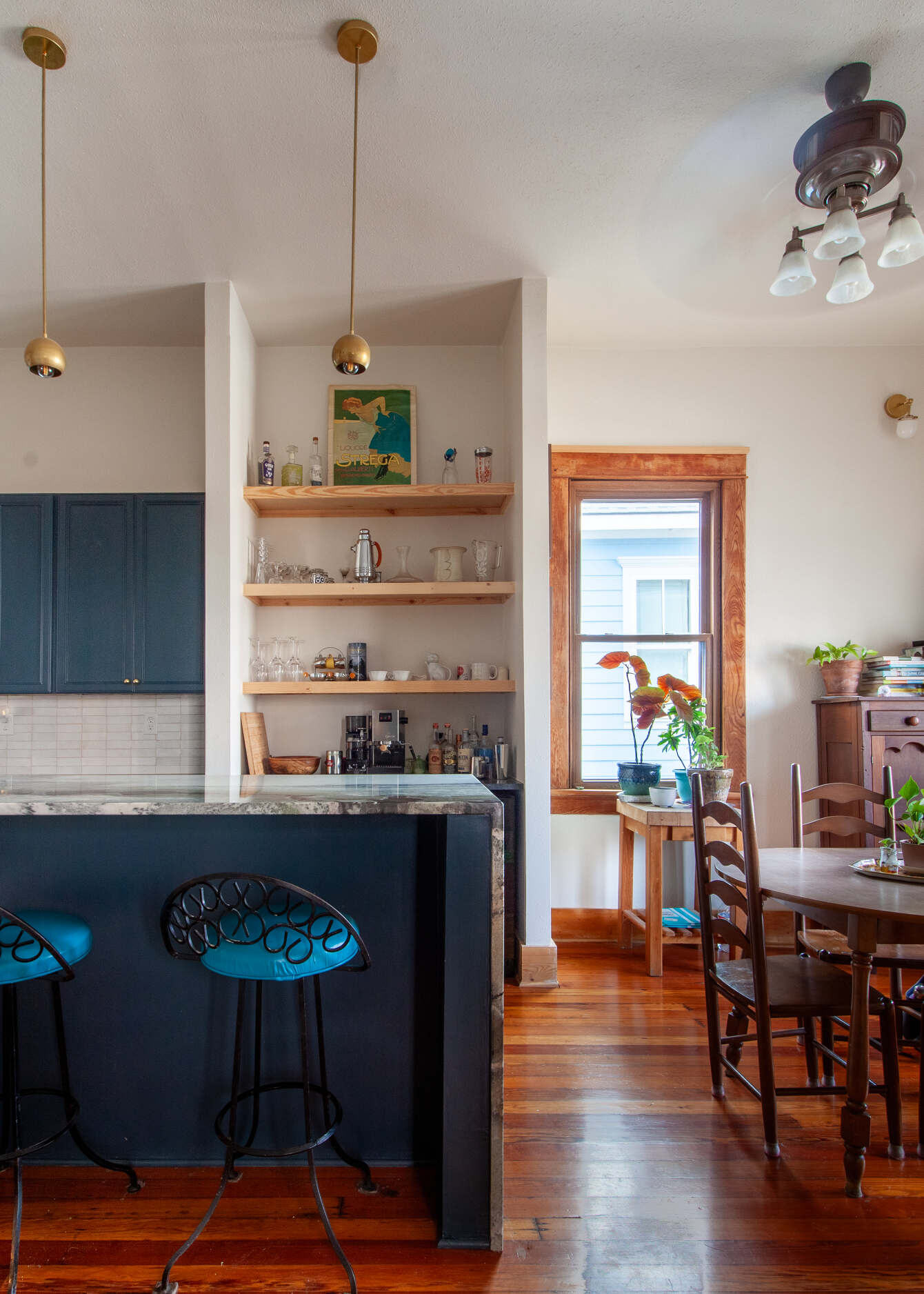 Interior view of a renovated kitchen with an stone covered island, kitchen table and tall ceilings.