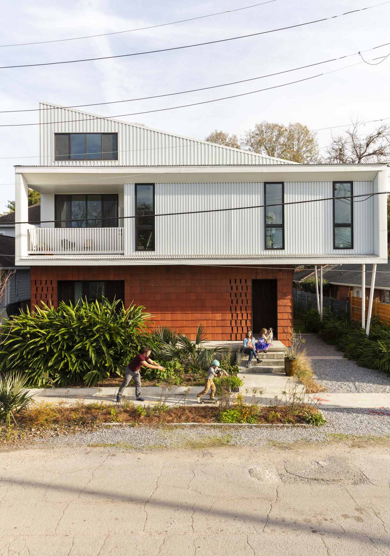 Front view of modern home with four-person family sitting on front porch and playing on sidewalk.