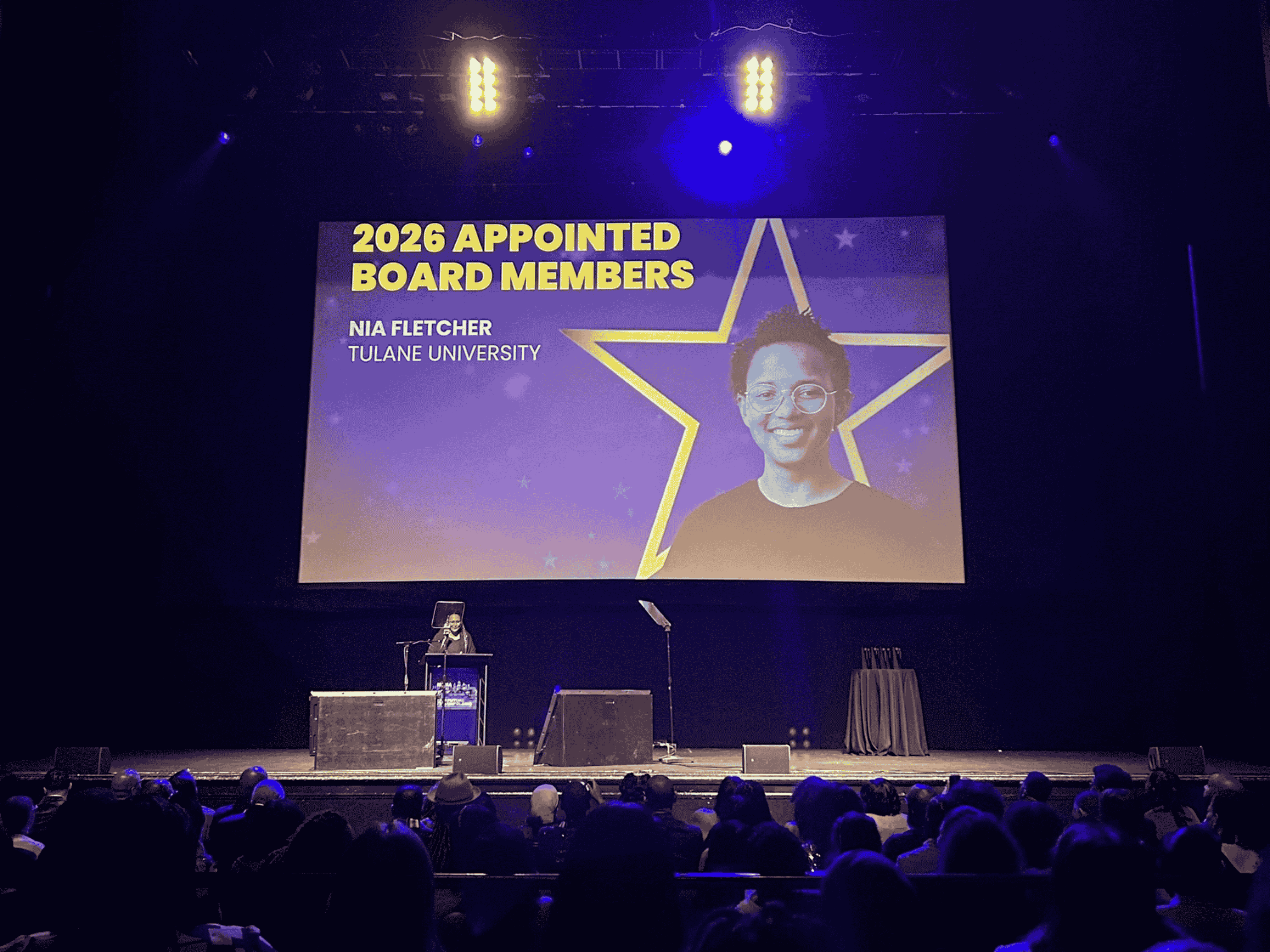 View of stage at NOMA conference with large screen projecting headshot of student Nia Fletcher.