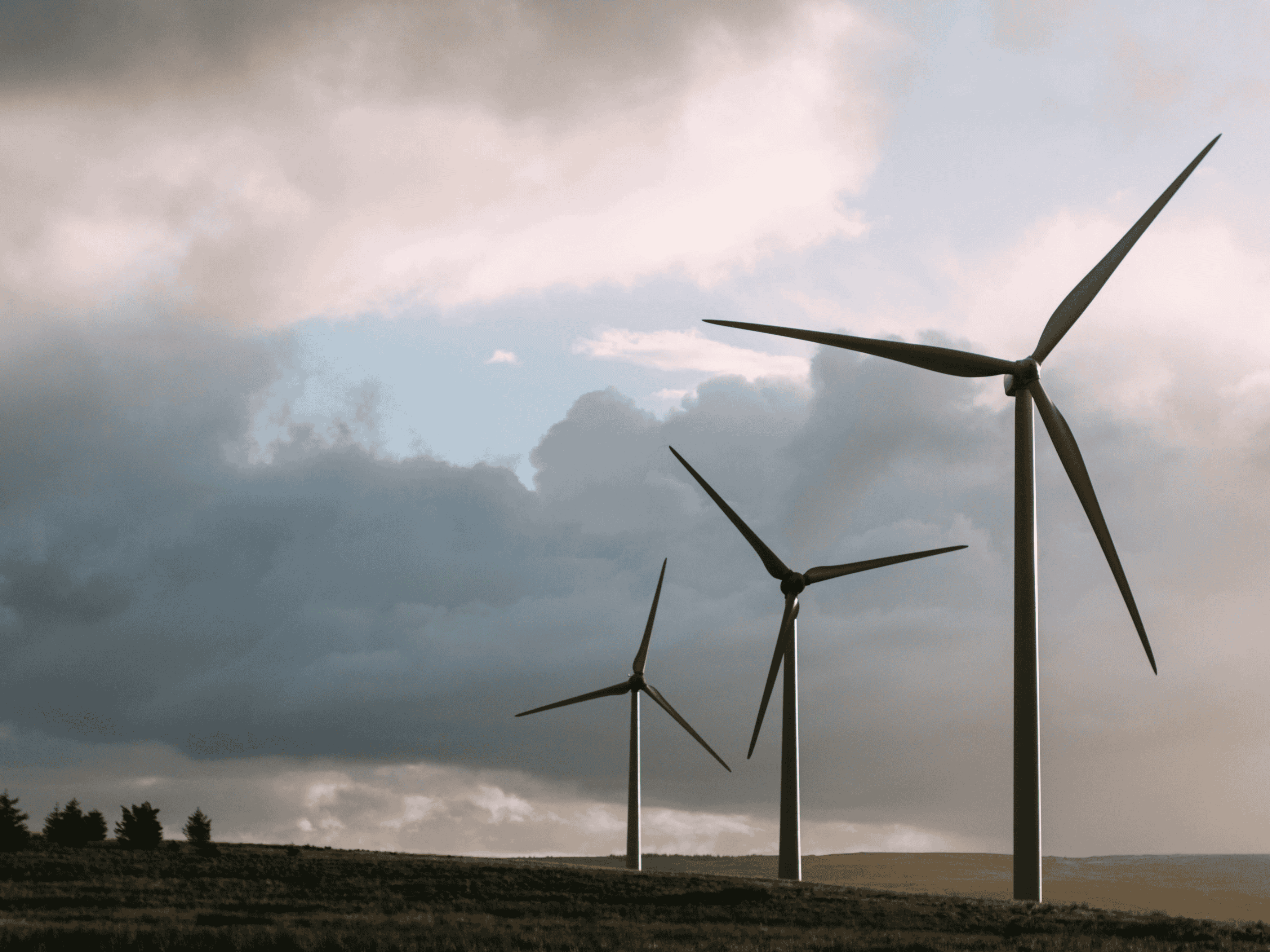 View of three wind turbines in foreground with storm clouds and a rural area in the background.