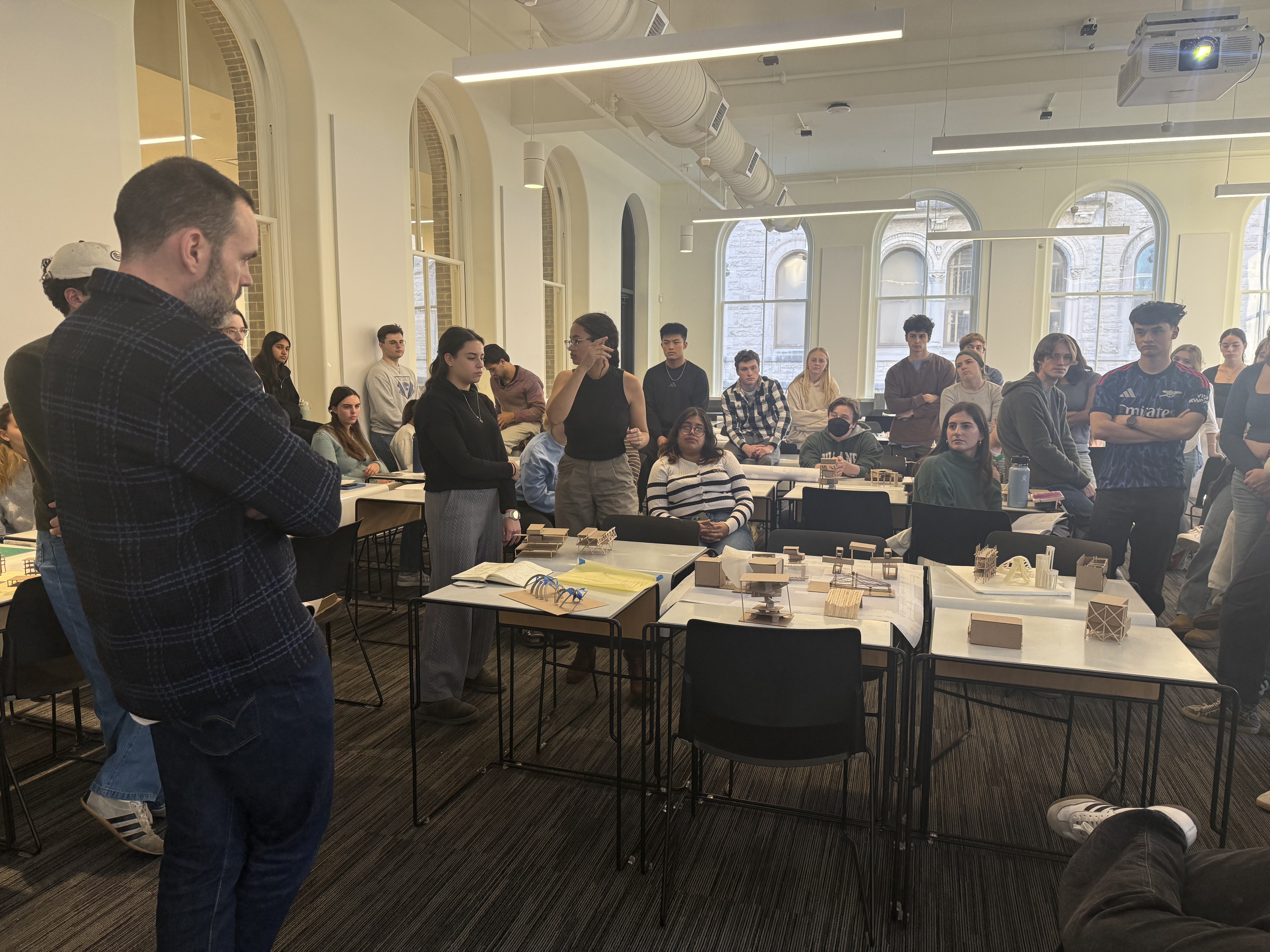Students surround workshop leaders and architectural models 