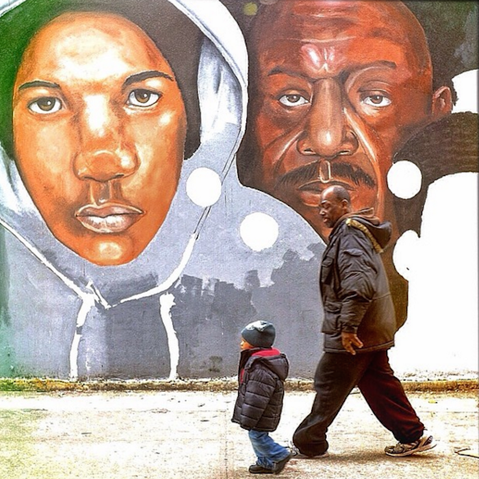 Side view of an adult and young child in thick winter coats walking on a sidewalk in front of a mural.